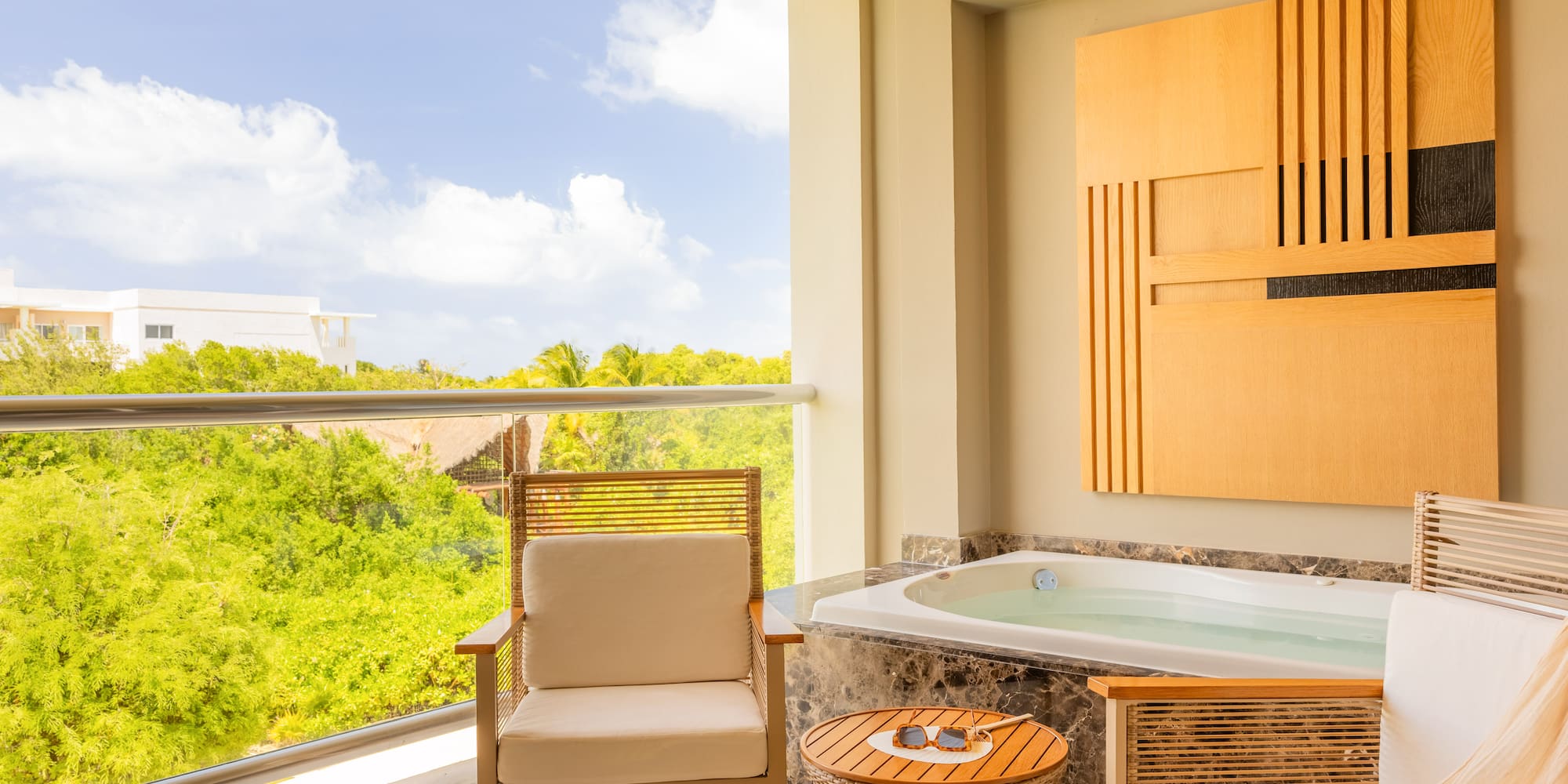 Hotel balcony with private outdoor jacuzzi, seating, and tropical view.