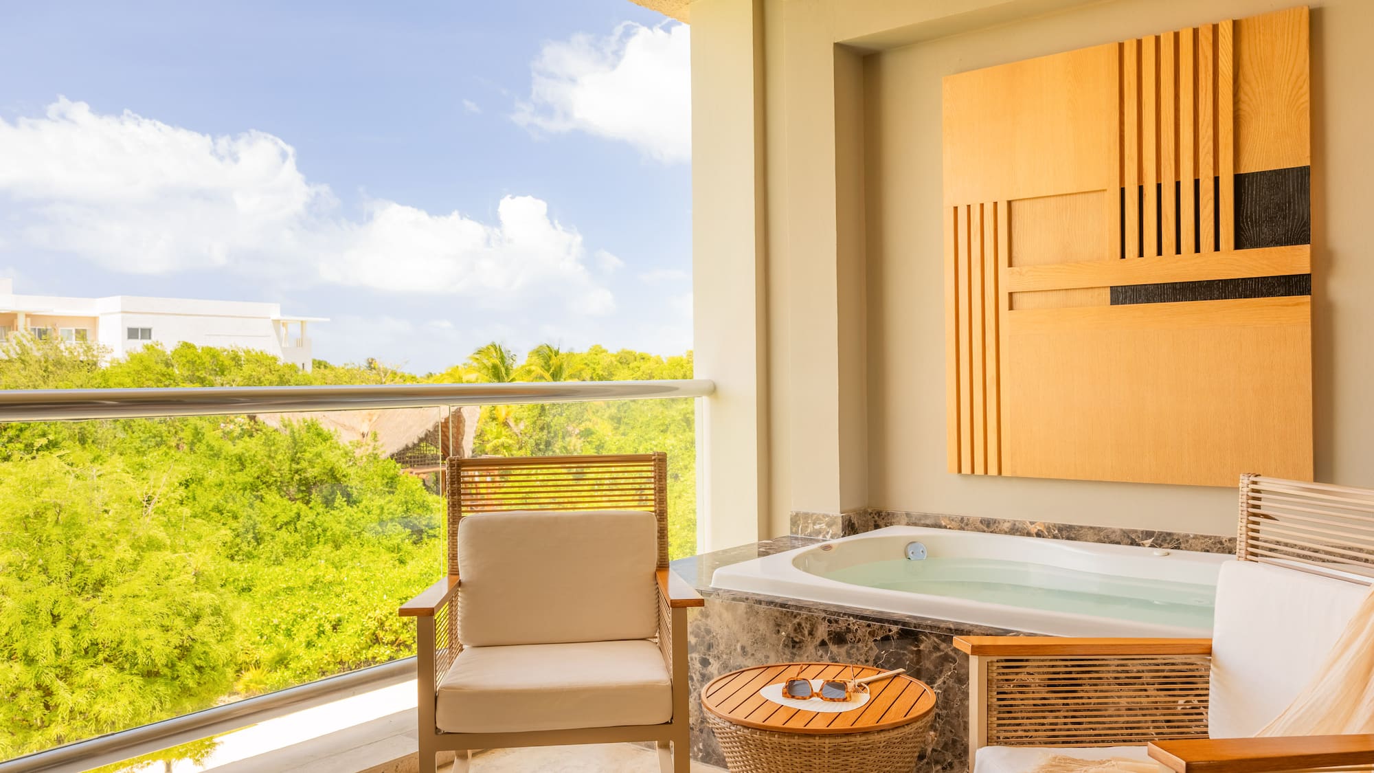 Hotel balcony with private outdoor jacuzzi, seating, and tropical view.