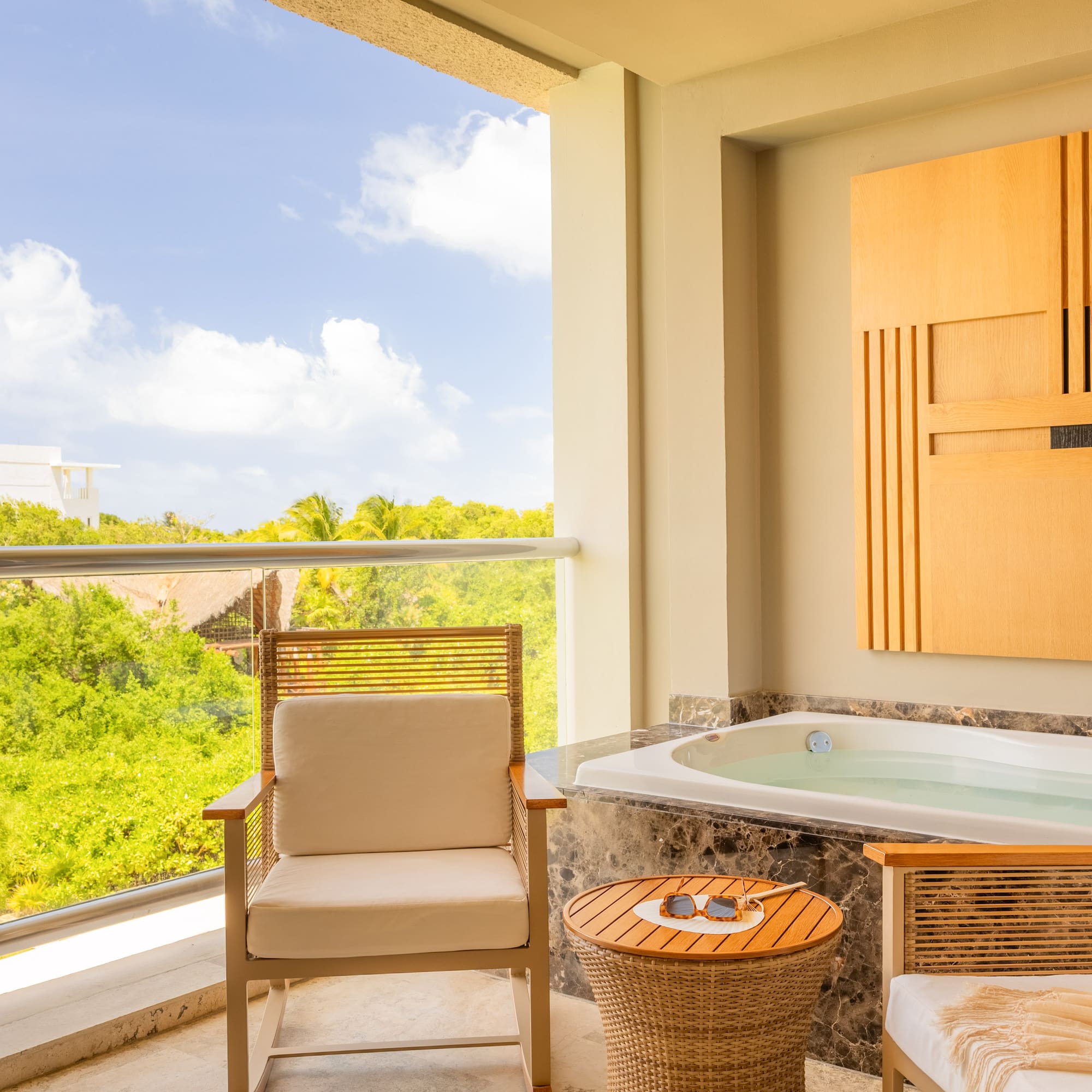 Hotel balcony with private outdoor jacuzzi, seating, and tropical view.