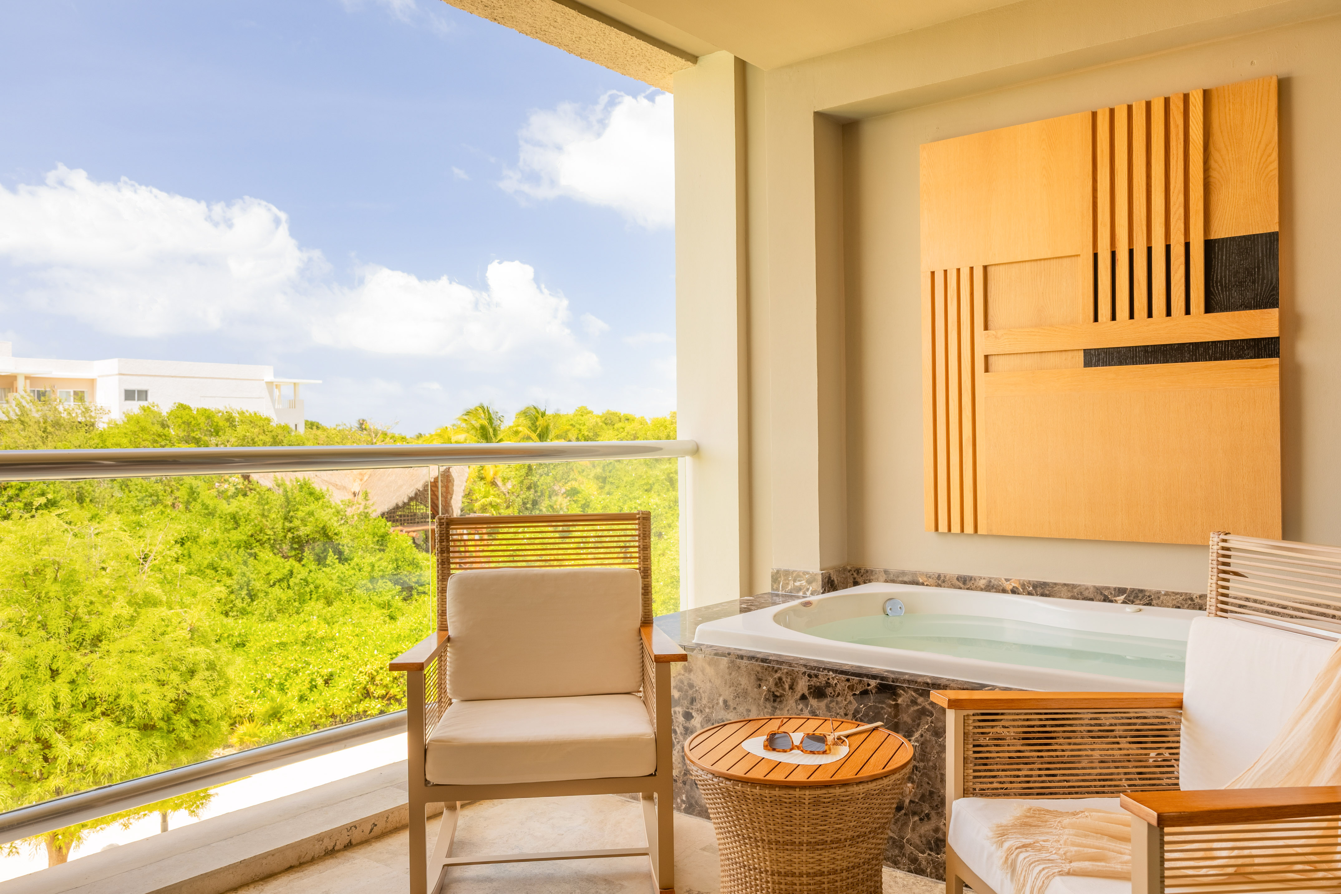 Hotel balcony with private outdoor jacuzzi, seating, and tropical view.