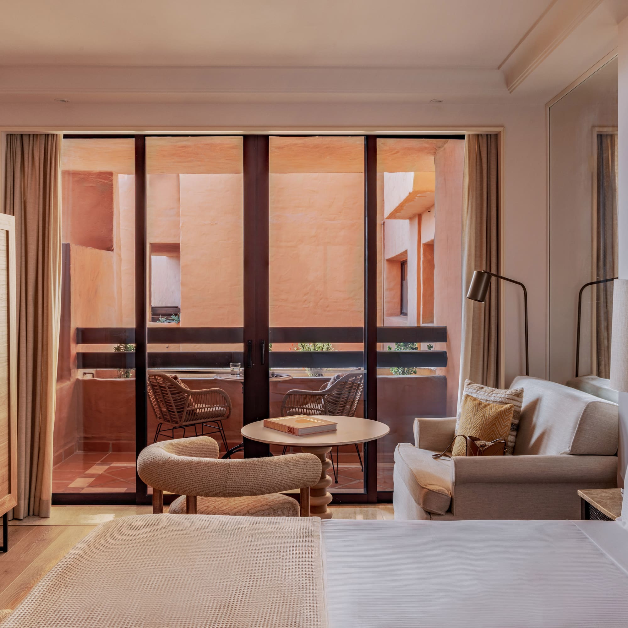 Resort hotel room with bed, sofa, and balcony view of terracotta buildings.