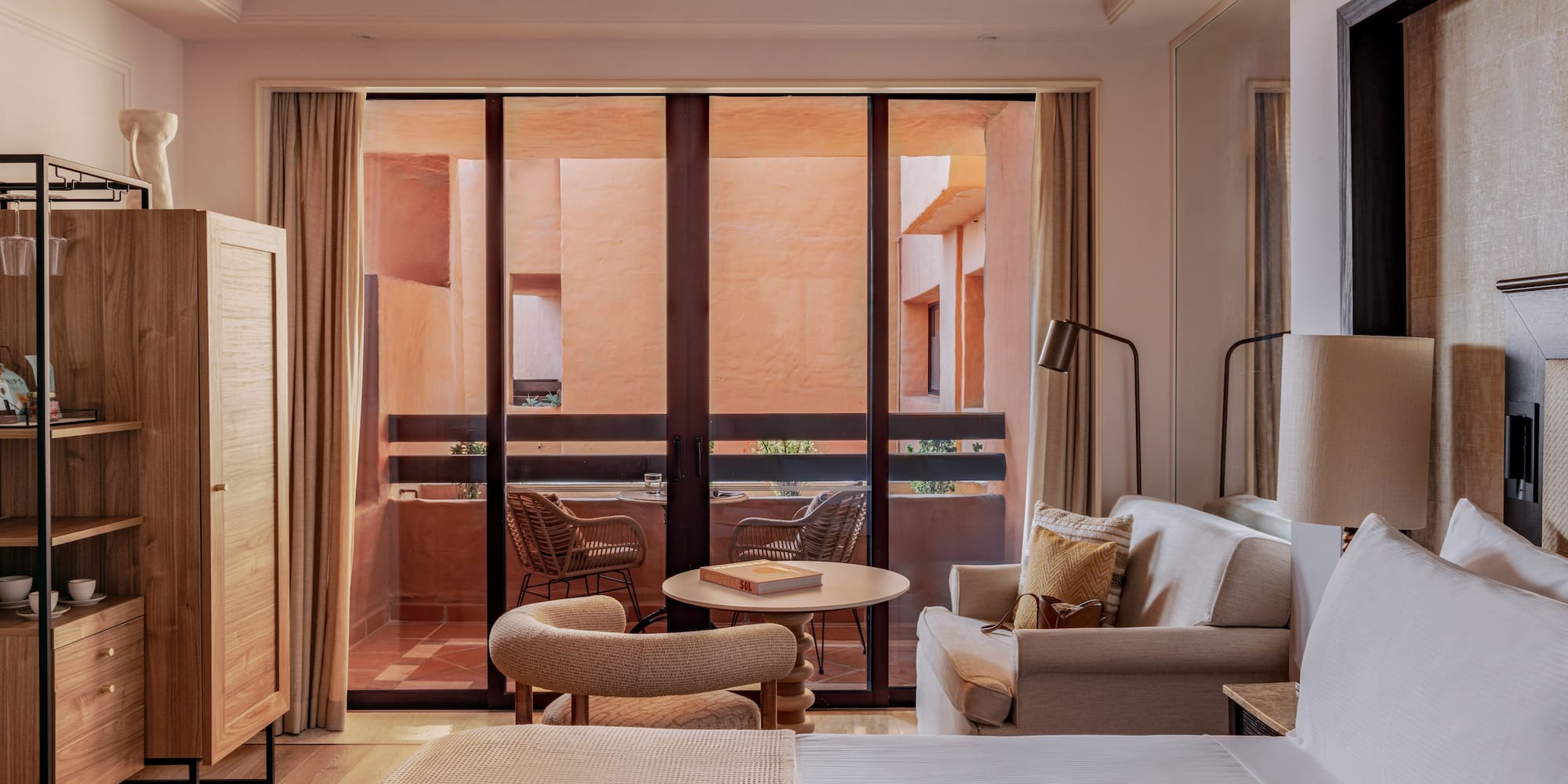 Hotel suite with bed, sofa, and balcony facing a warm terracotta courtyard.