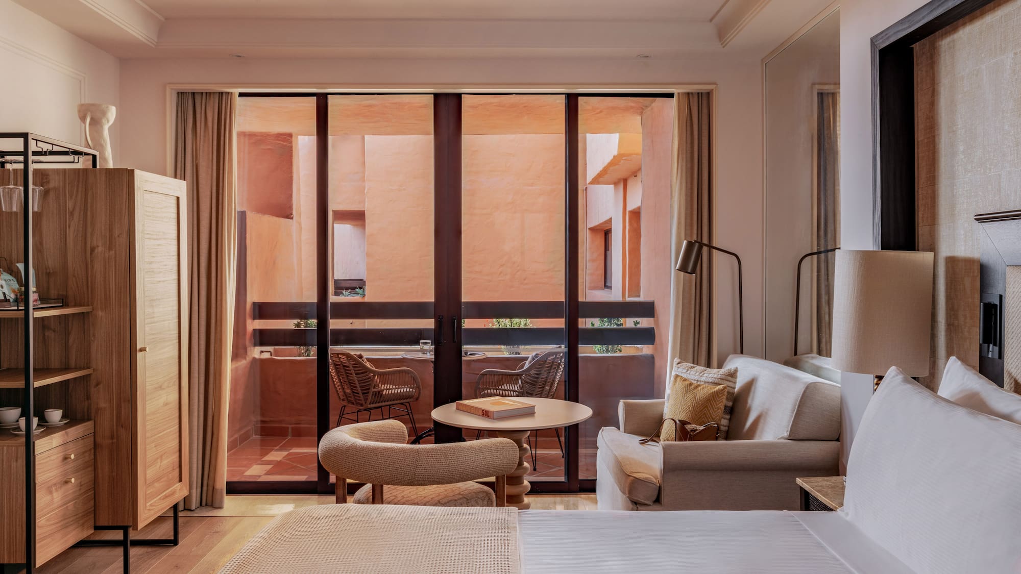 Hotel suite with bed, sofa, and balcony facing a warm terracotta courtyard.