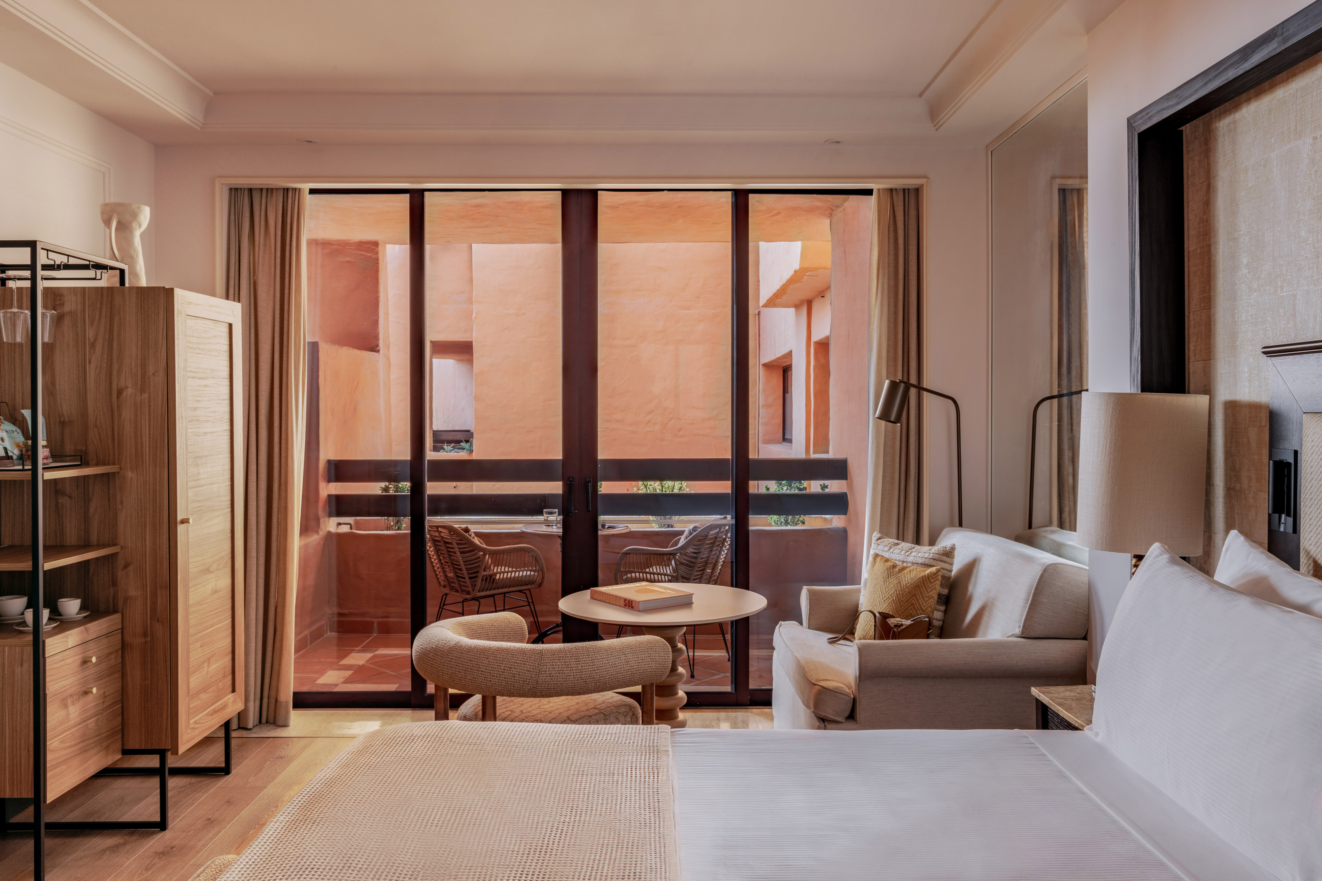 Resort hotel room with bed, sofa, and balcony view of terracotta buildings.
