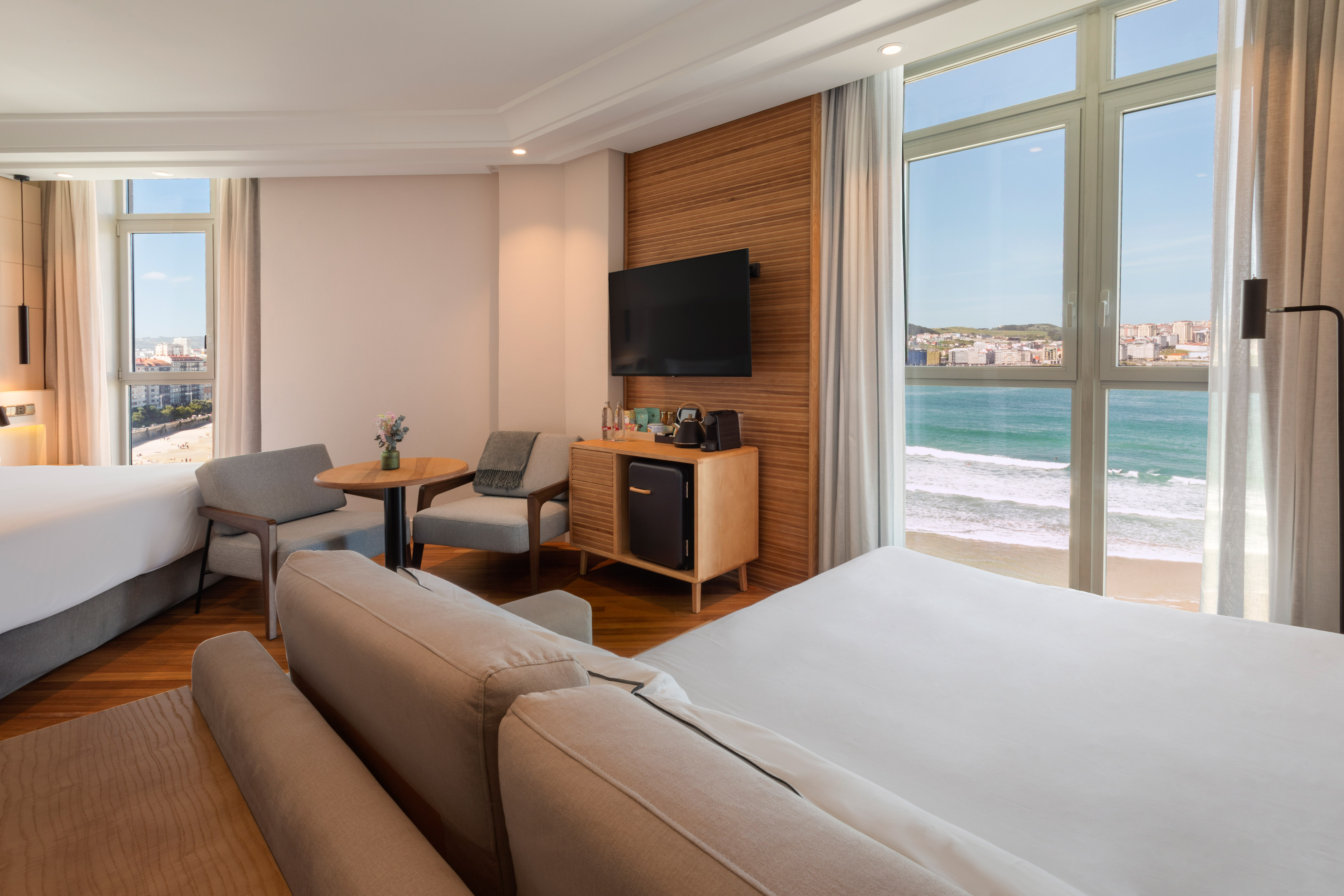 Hotel room overlooking beach and ocean, with modern decor and two beds.