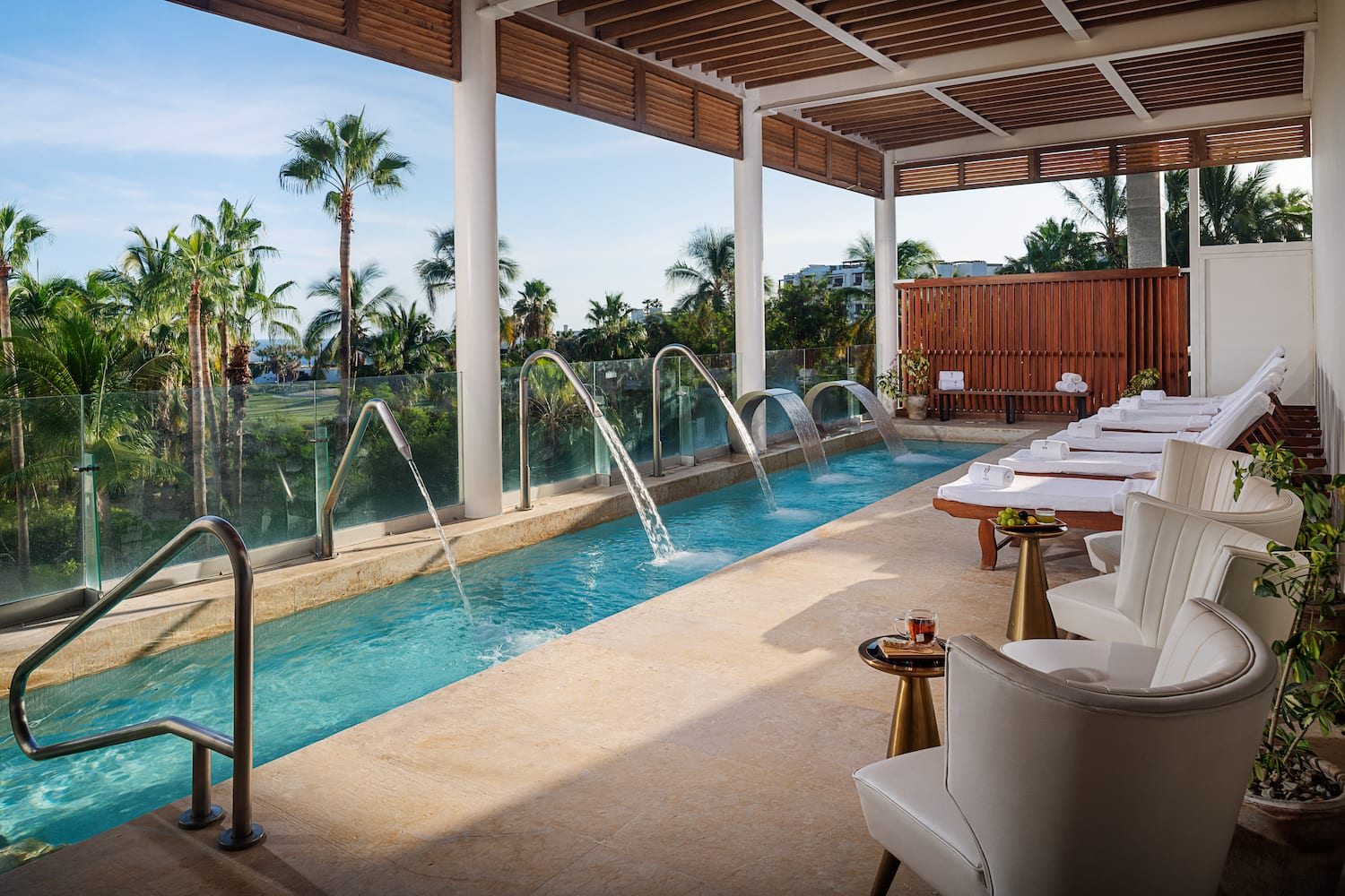 a pool with water jets and chairs in a room with a pool and chairs