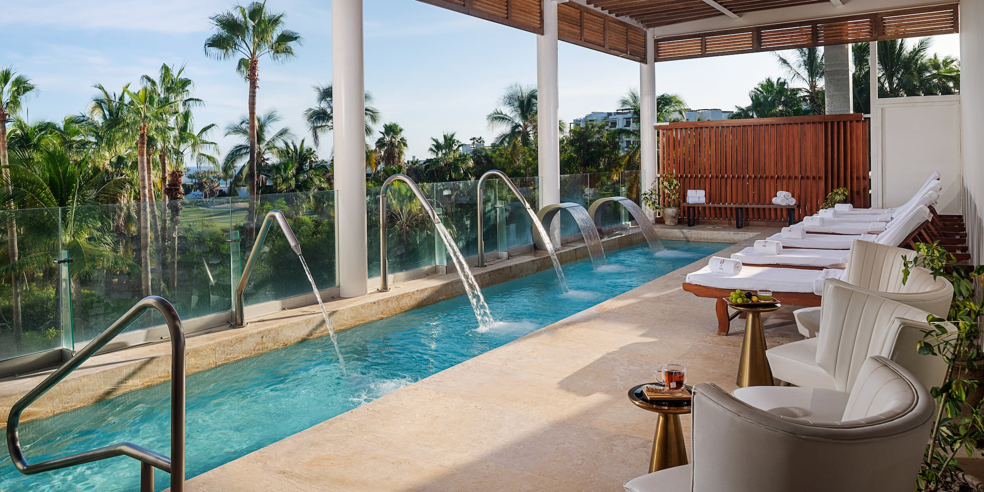a pool with water jets and chairs in a room with a pool and chairs