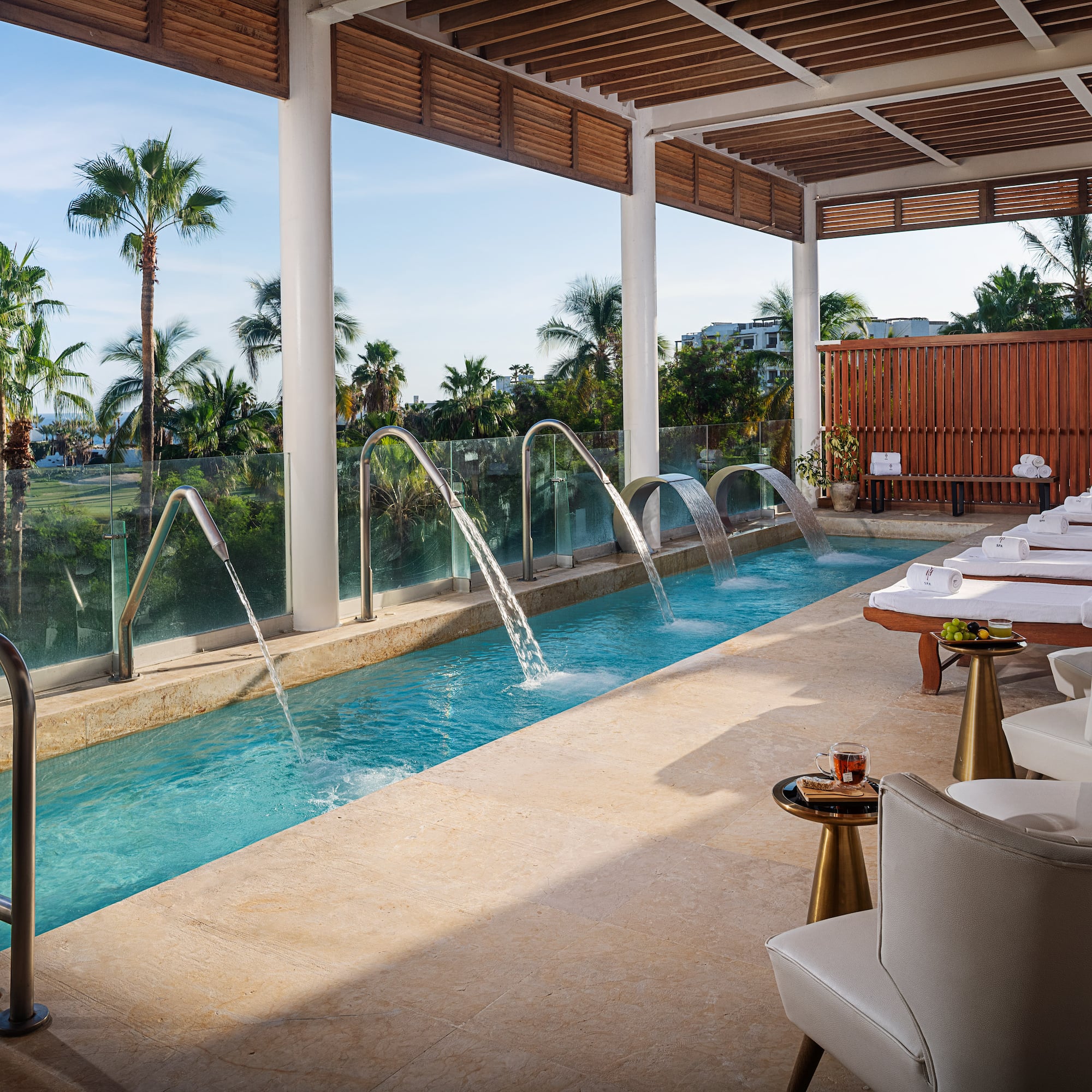 a pool with water jets and chairs in a room with a pool and chairs