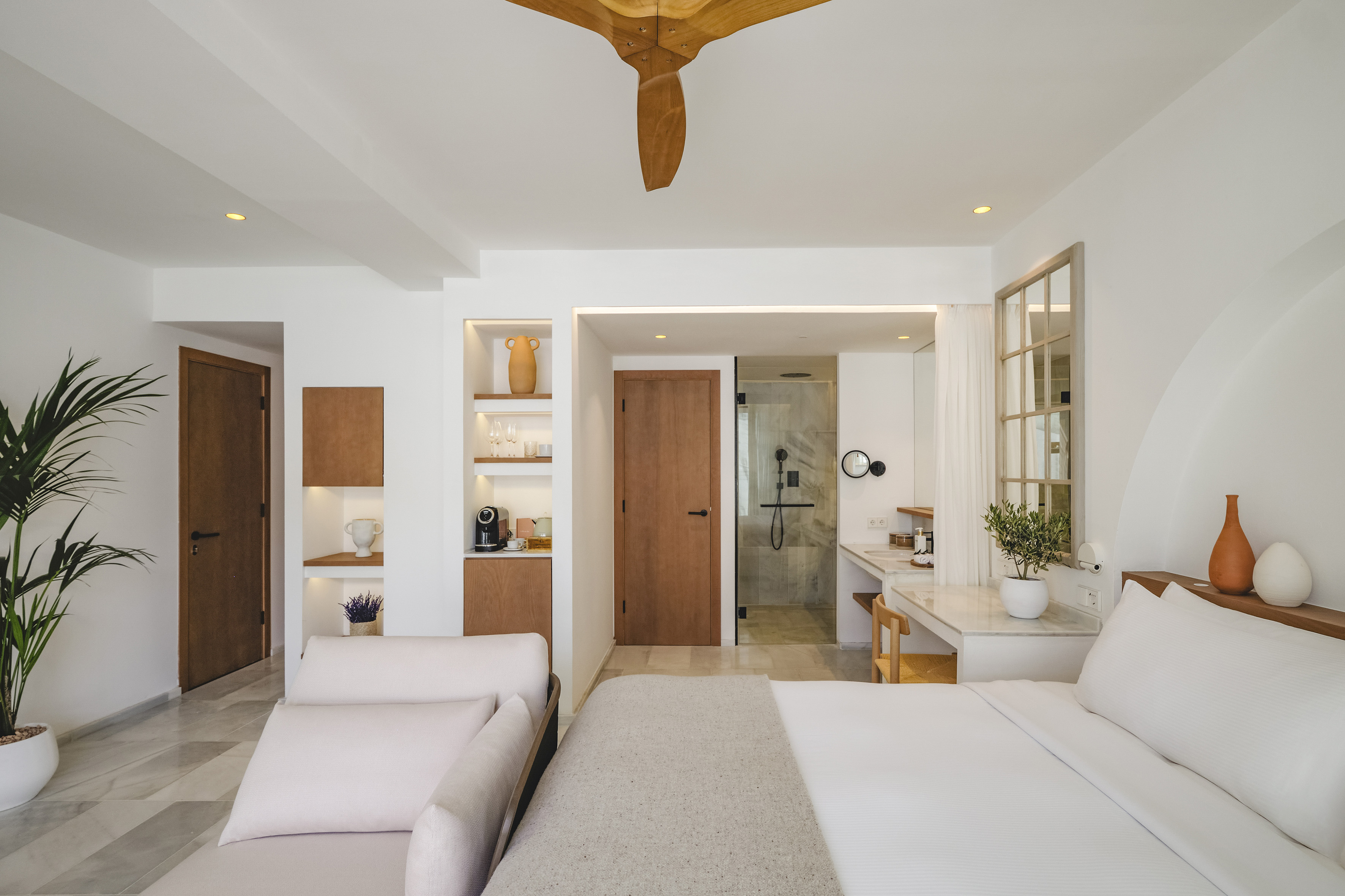 Modern luxury hotel bedroom with white walls, wood accents, and integrated shower.
