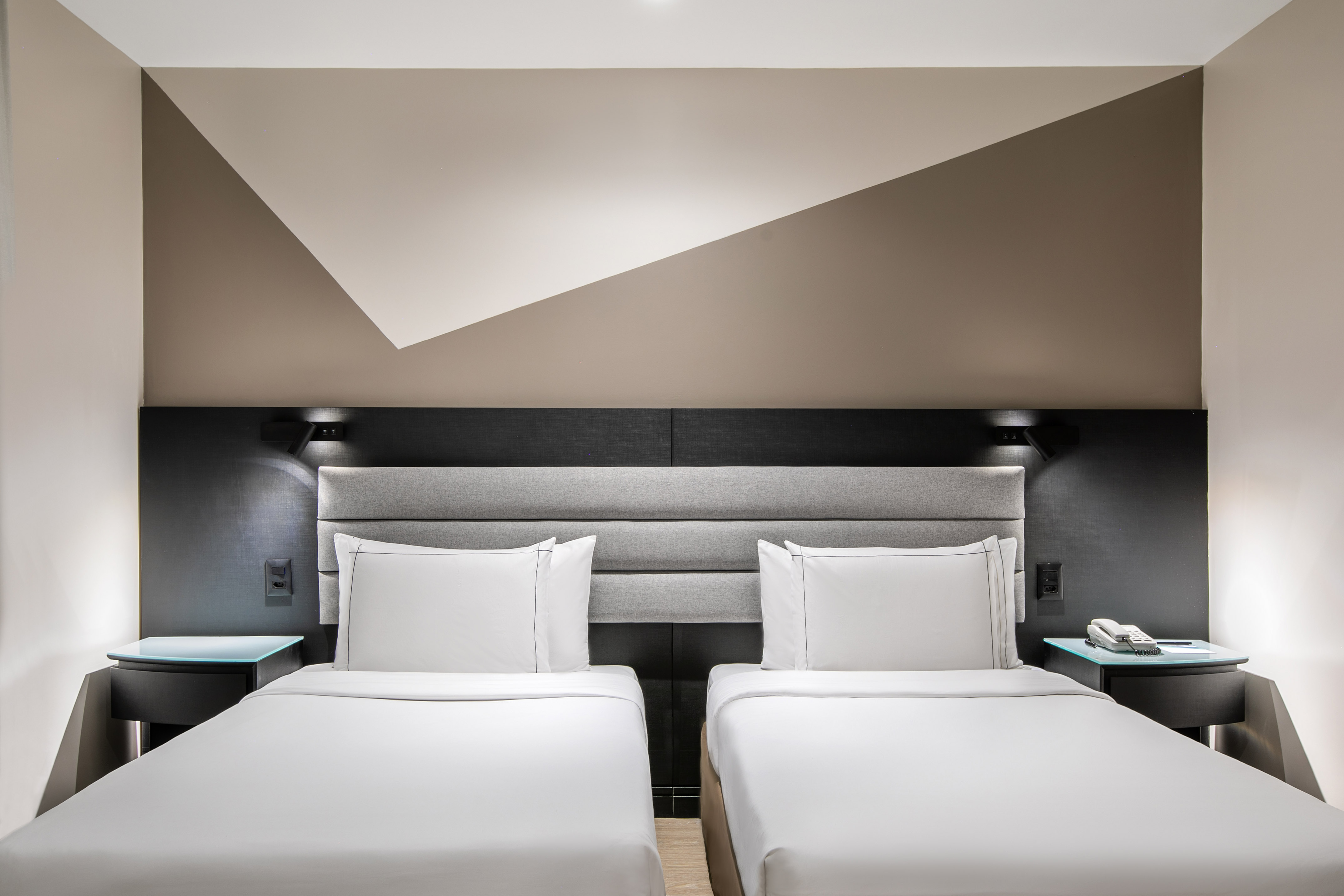 Modern hotel room with twin beds, geometric accent wall, and bedside tables.
