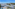 Sunny resort hotel with large swimming pool, palm trees, and tennis court.