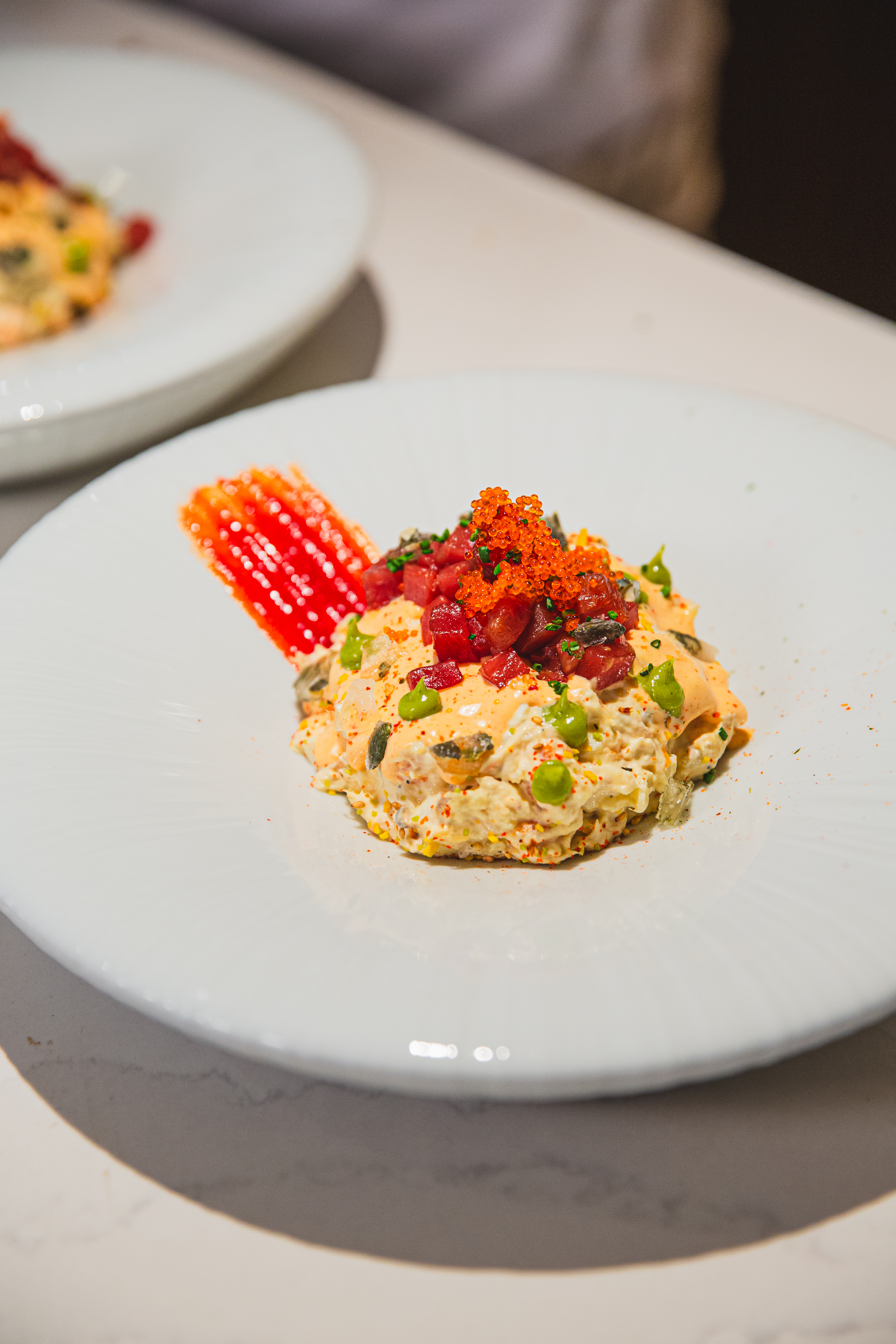 Gourmet salad with tuna tartare, orange roe, green peas, and red sauce.