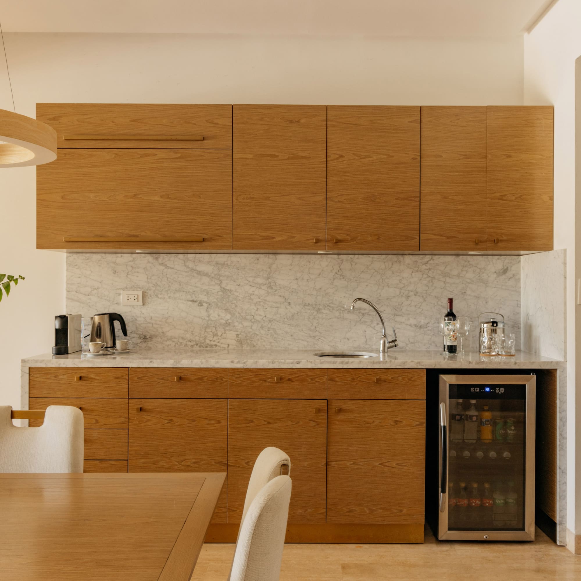 Modern kitchenette with oak cabinets, marble countertop, and wine fridge.
