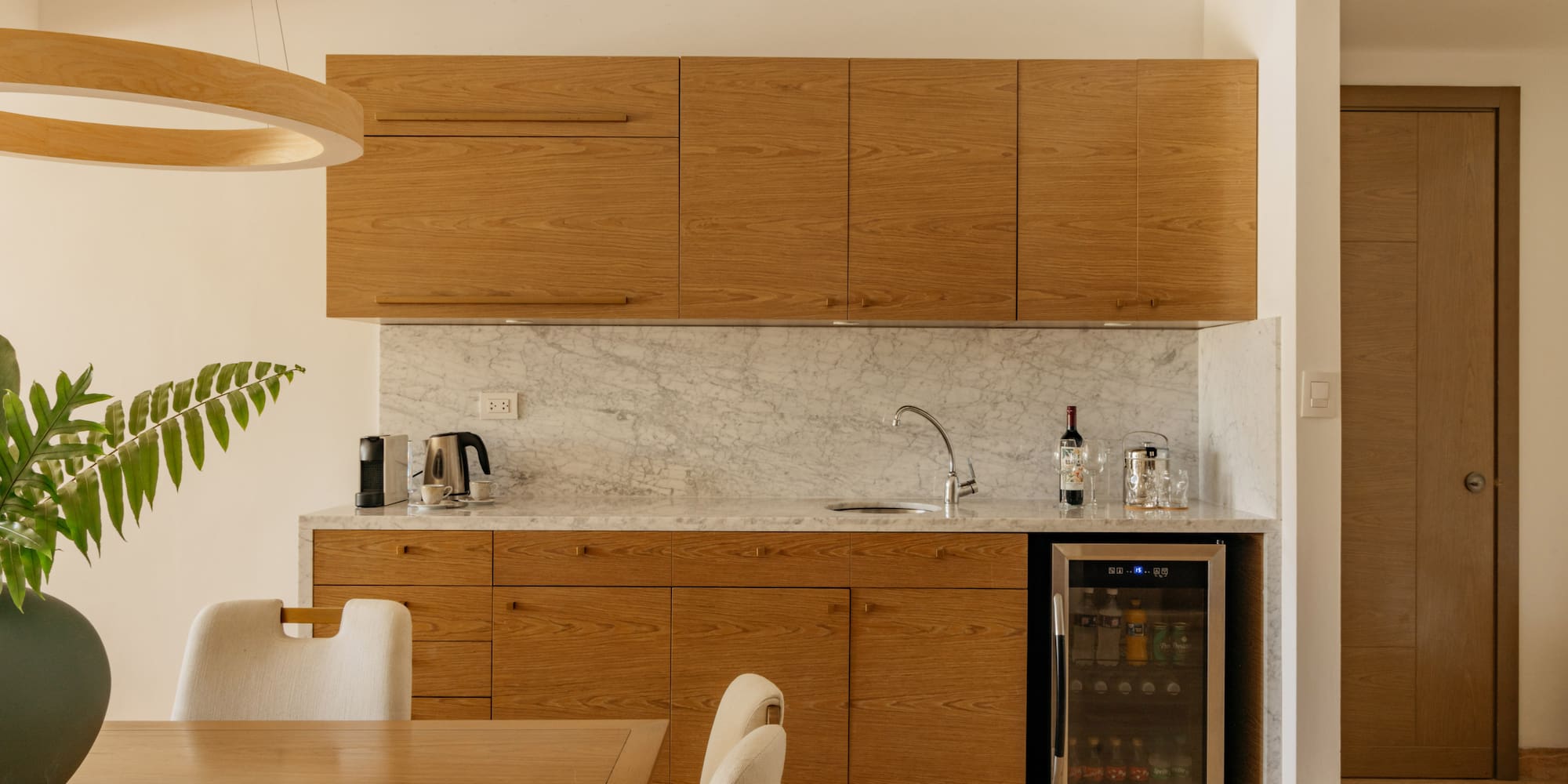 Modern kitchenette with oak cabinets, marble countertop, and wine fridge.