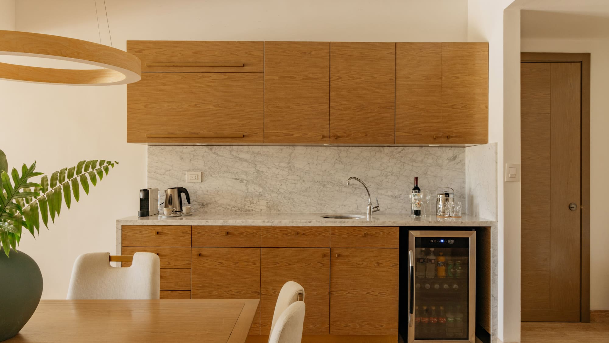 Modern kitchenette with oak cabinets, marble countertop, and wine fridge.