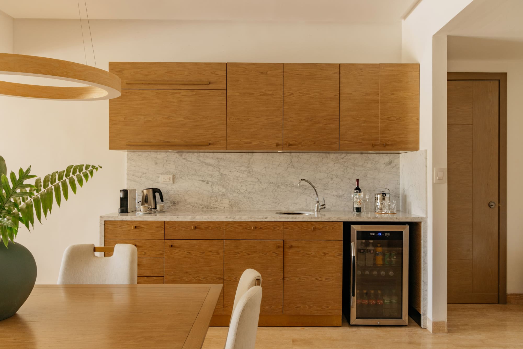 Modern kitchenette with oak cabinets, marble countertop, and wine fridge.