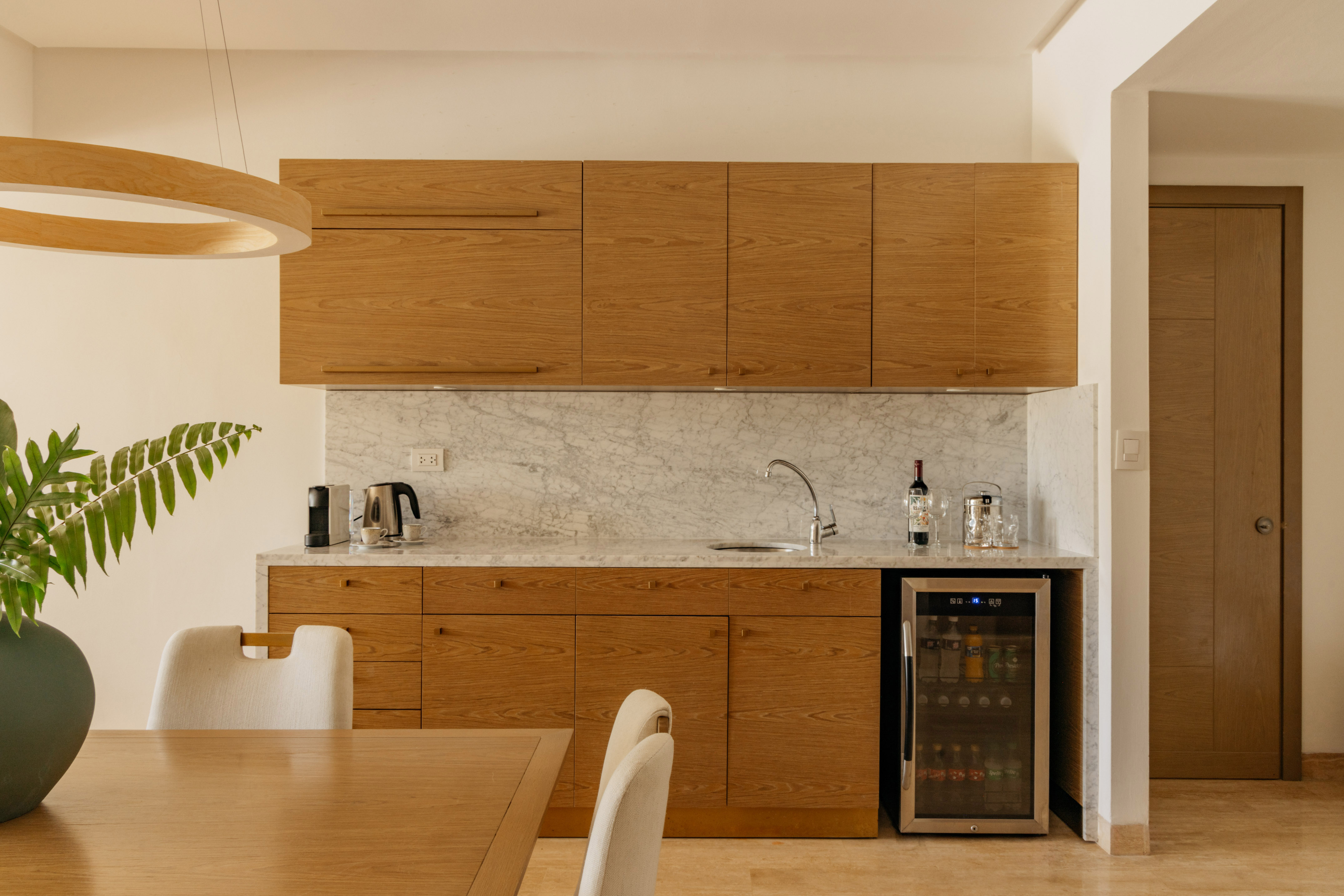 Modern kitchenette with oak cabinets, marble countertop, and wine fridge.