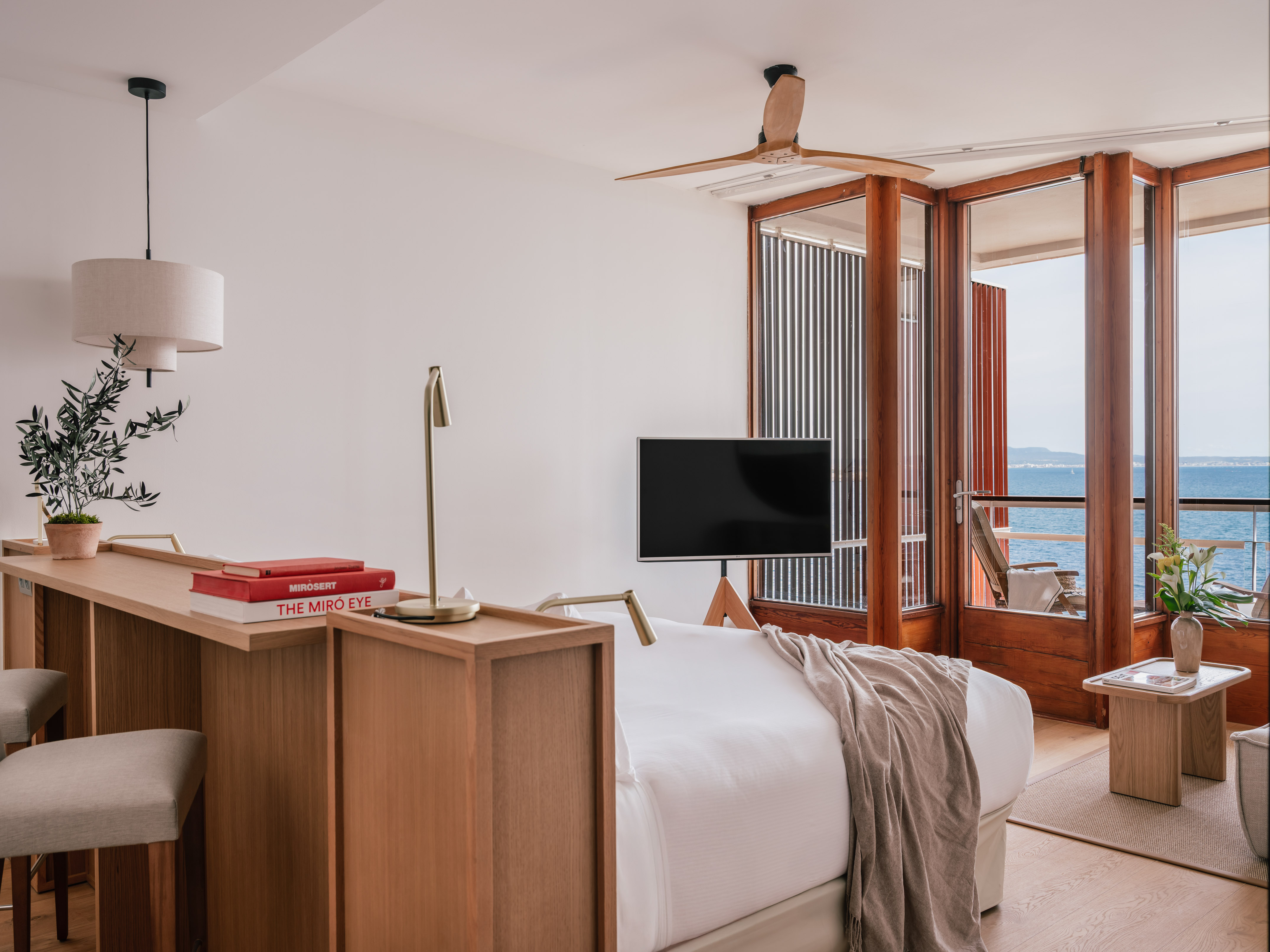 Modern hotel bedroom with ocean view, sleek wooden fan, and minimalist design.