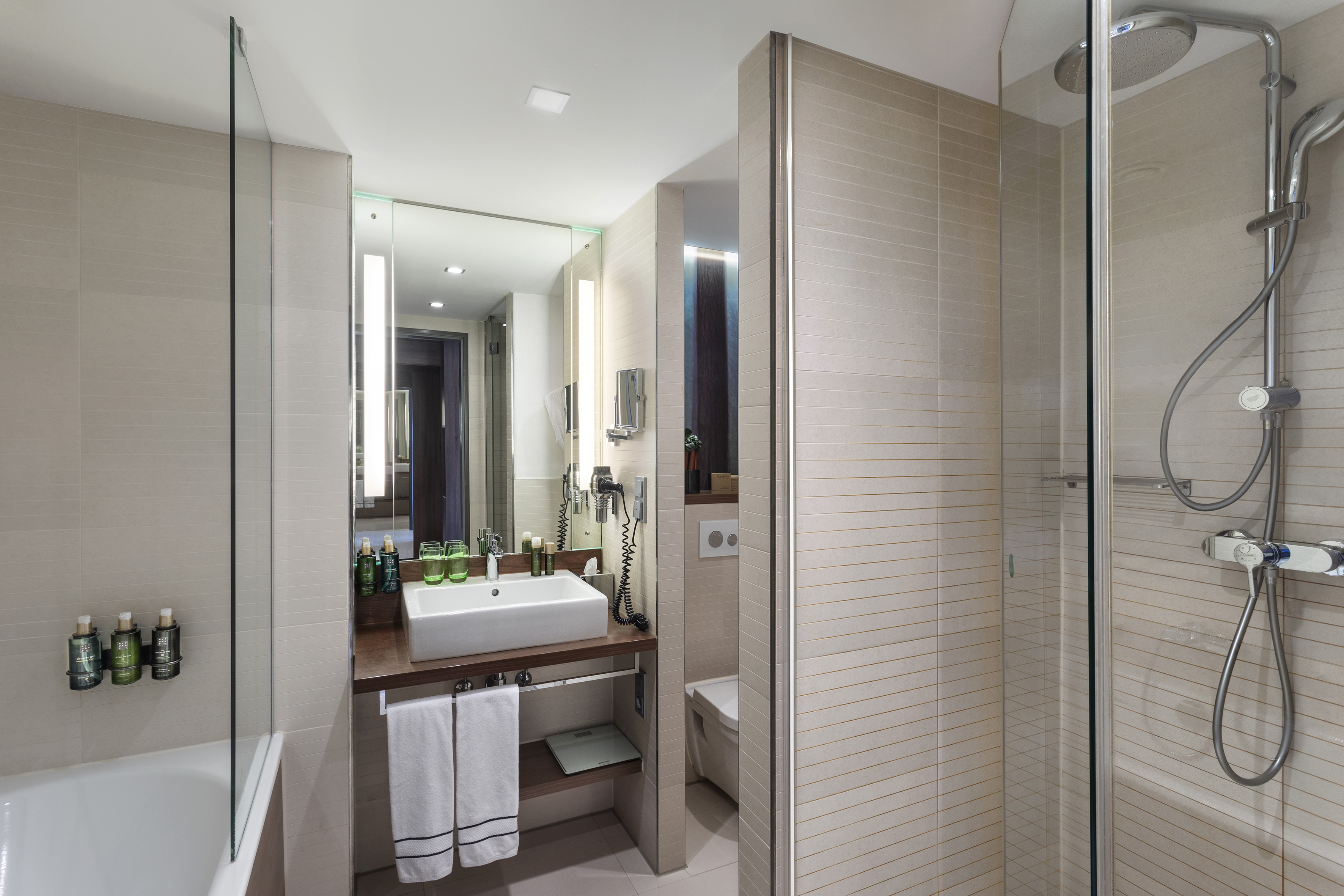 Bright modern bathroom with shower, bathtub, vanity, and lit mirror.