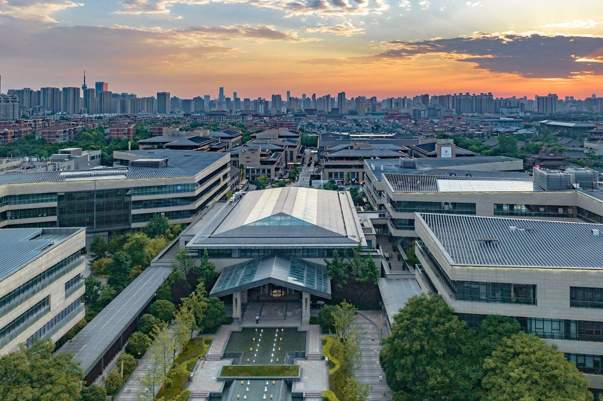 Aerial view: Modern complex, traditional roofs, urban skyline at sunset.