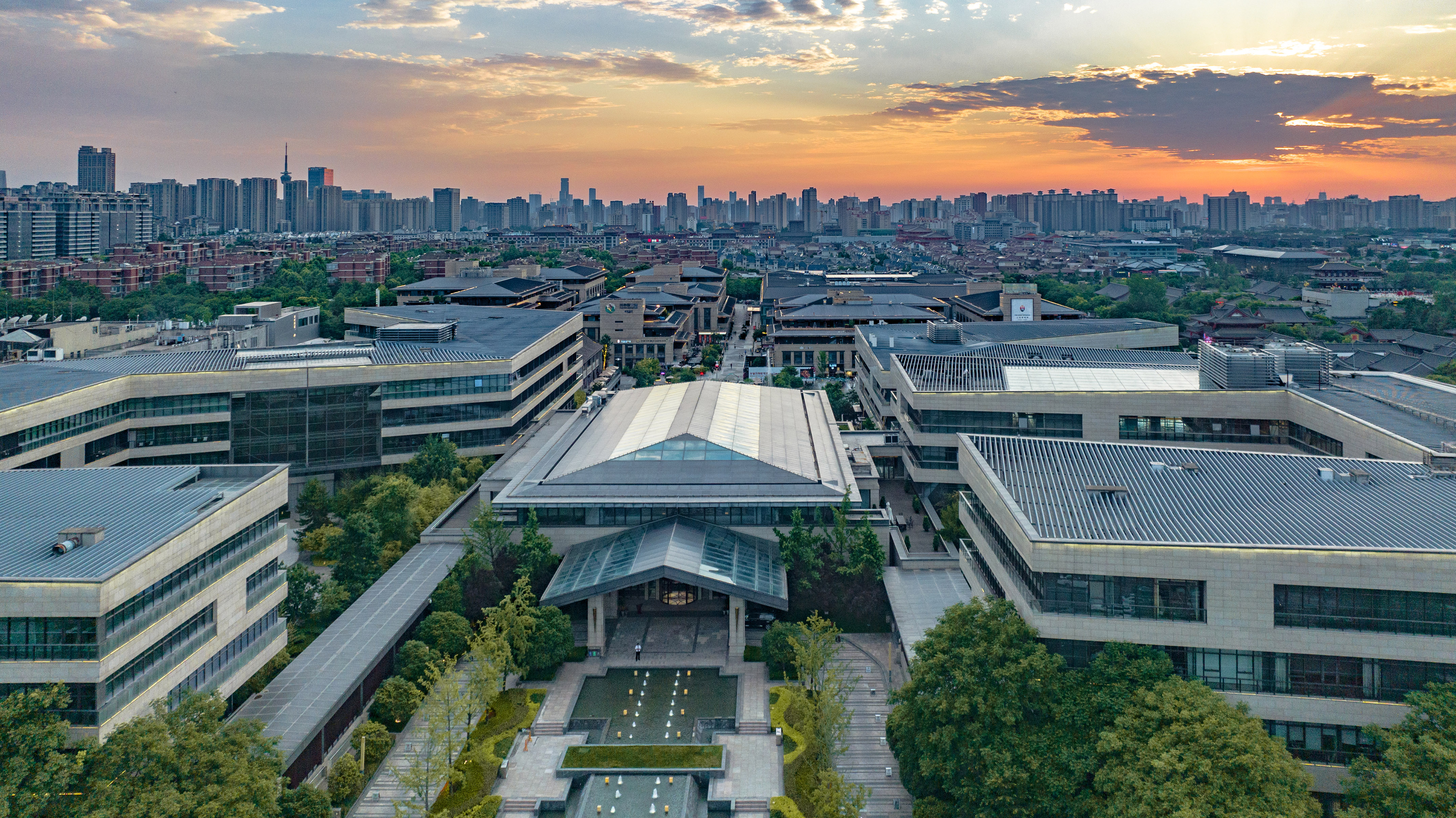 Aerial view: Modern complex, traditional roofs, urban skyline at sunset.