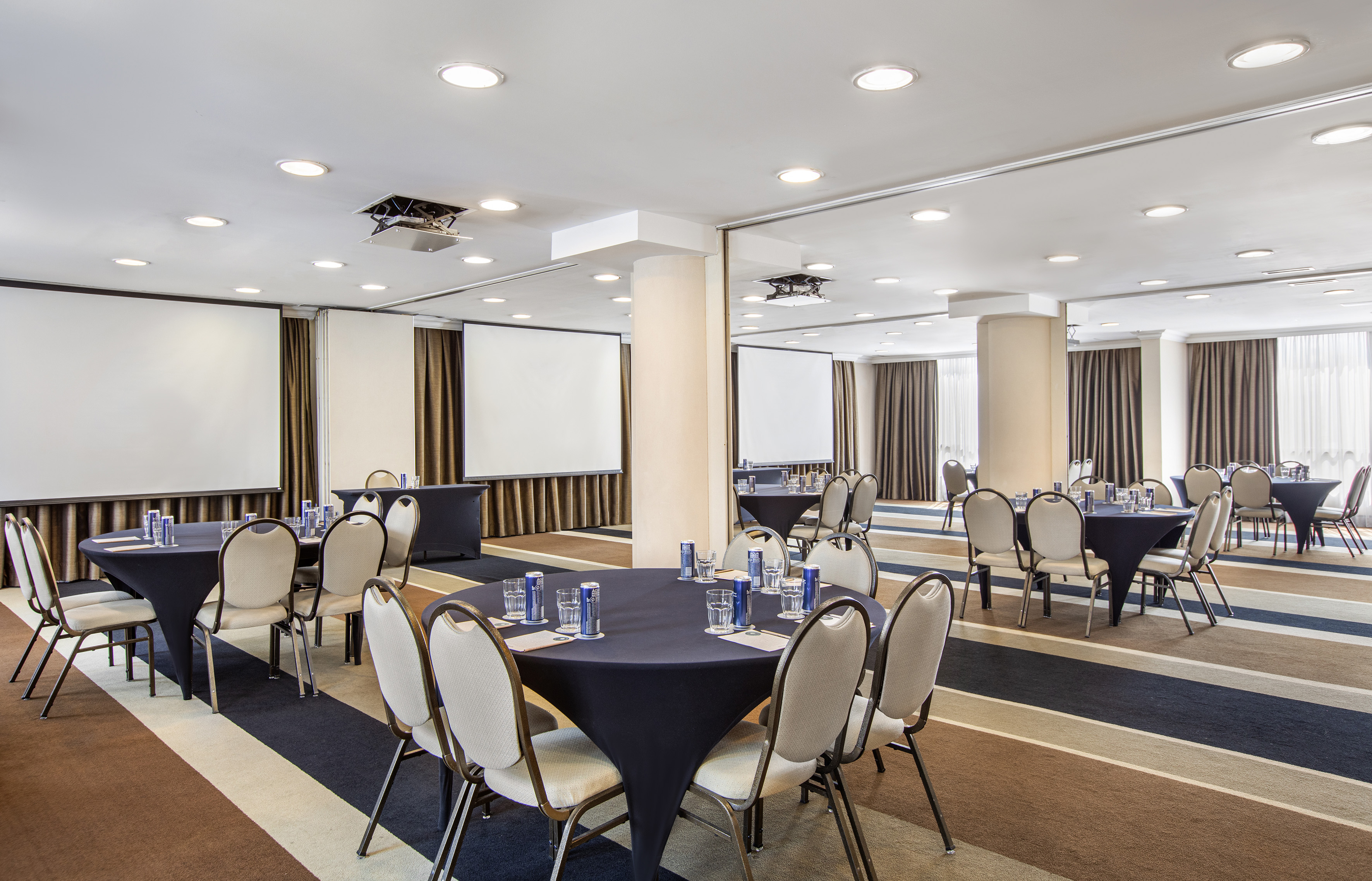 Meeting room with round tables, projector screens, chairs, and striped carpet.
