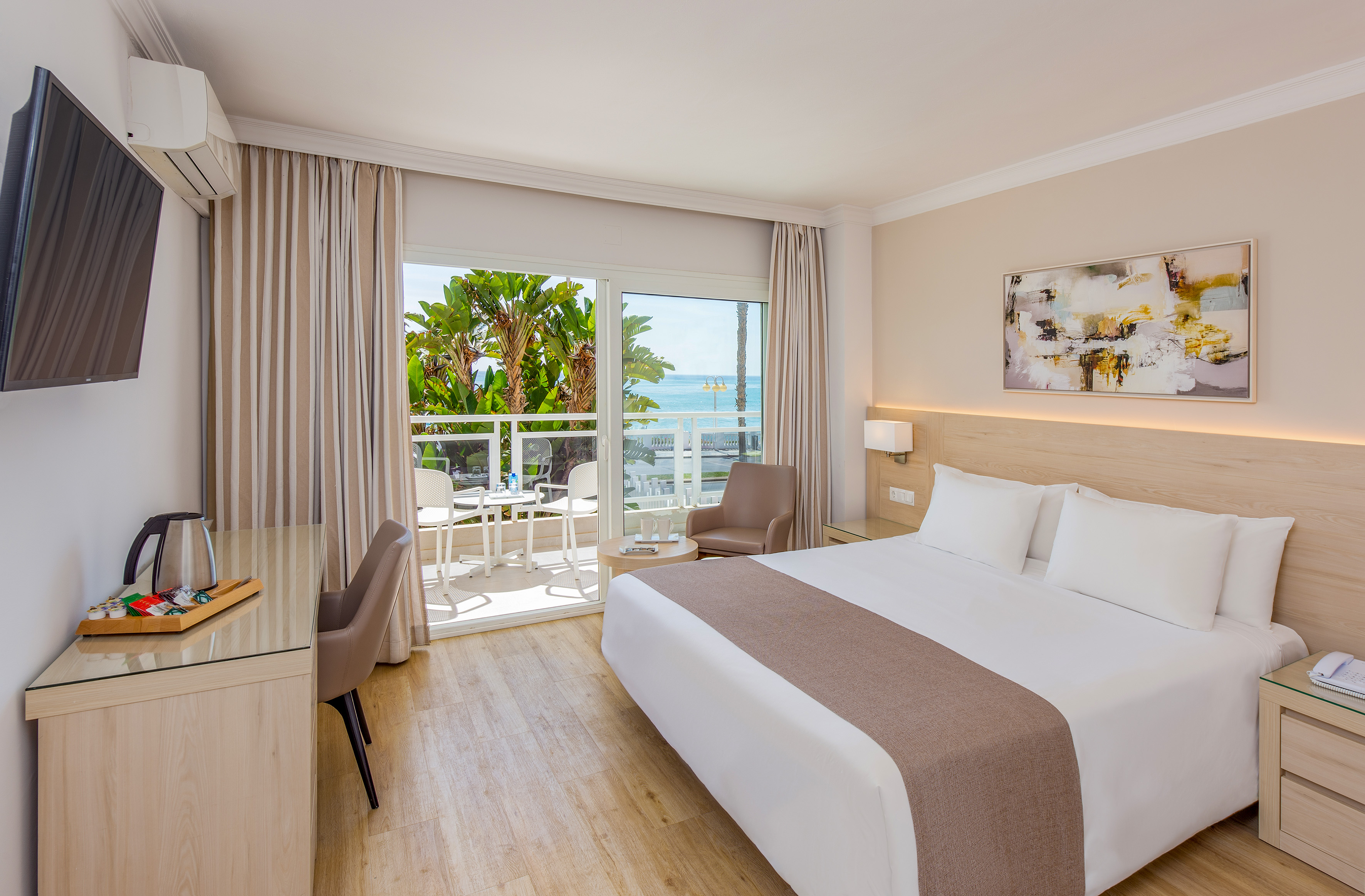 Bright hotel room with sea view balcony, king bed, and modern furnishings.