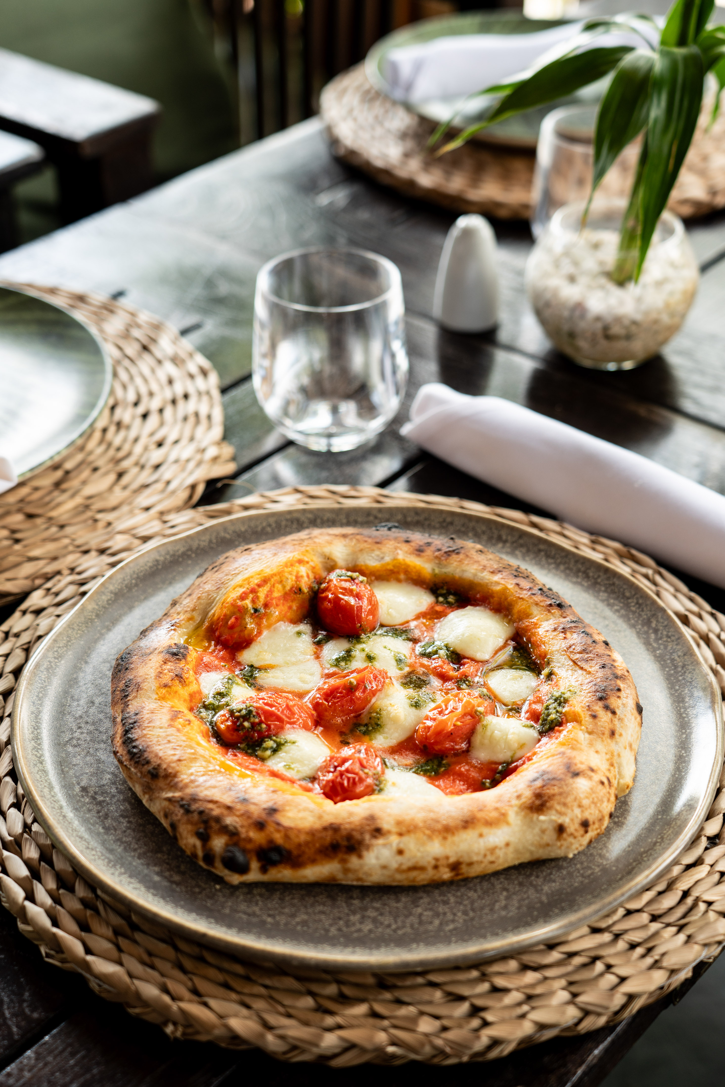 Neapolitan pizza with cherry tomatoes, mozzarella, and pesto on rustic plate.