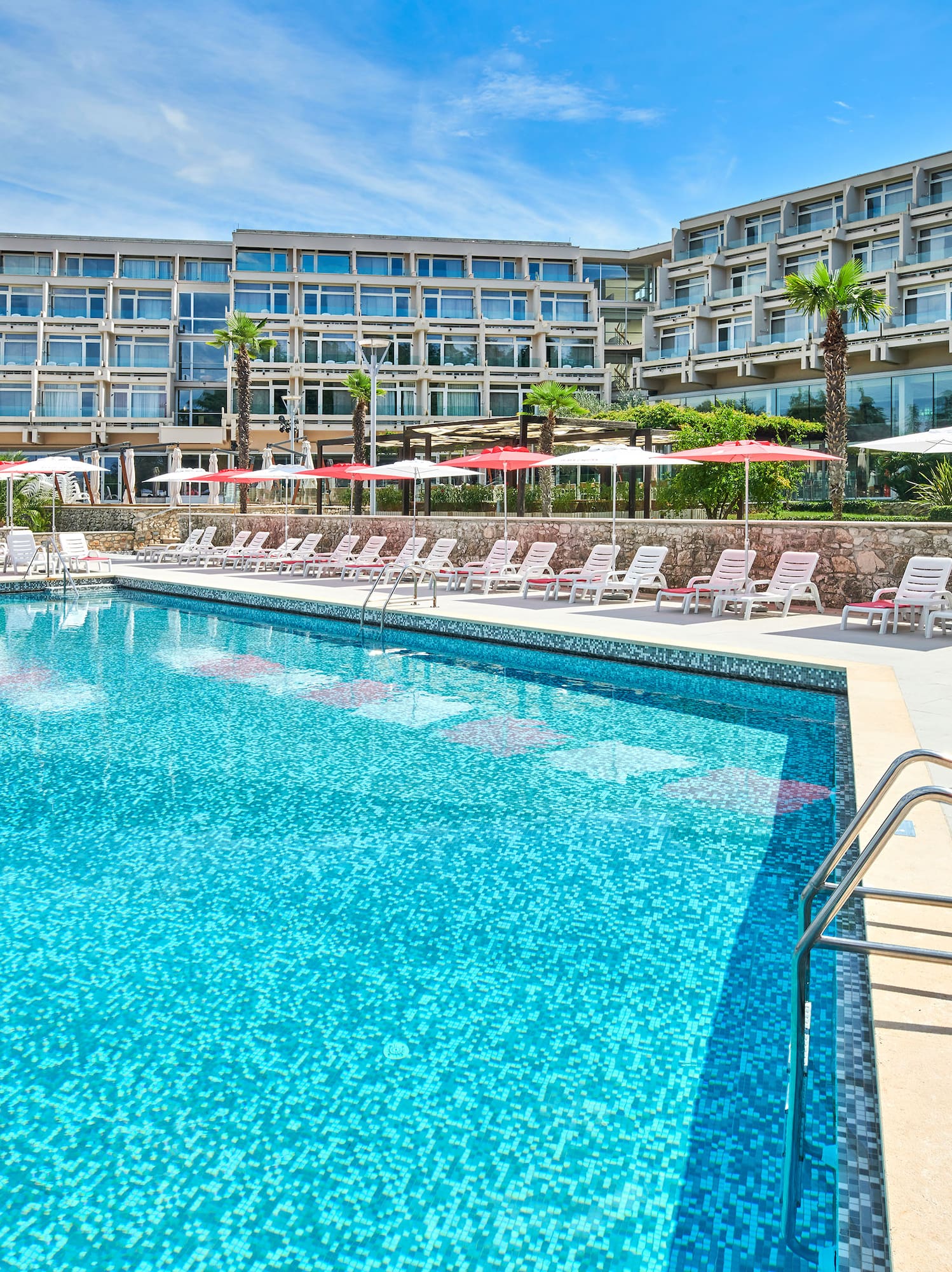 a pool with umbrellas and chairs in front of a hotel