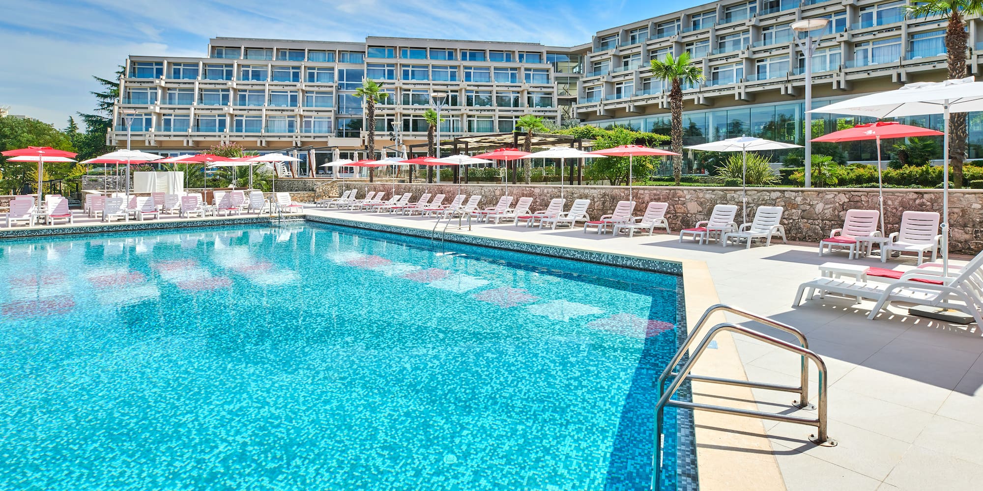 a pool with umbrellas and chairs in front of a hotel