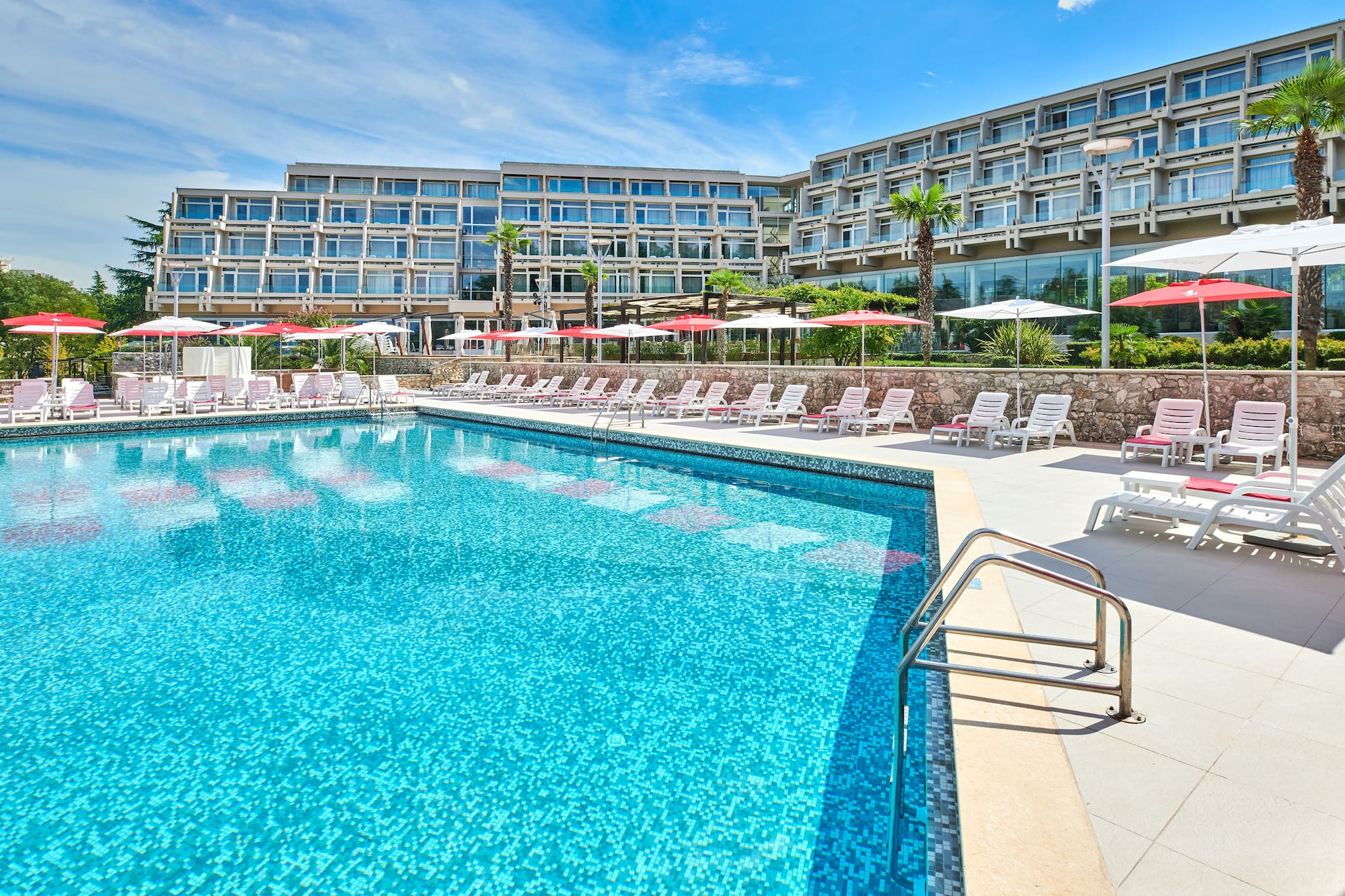 a pool with umbrellas and chairs in front of a hotel