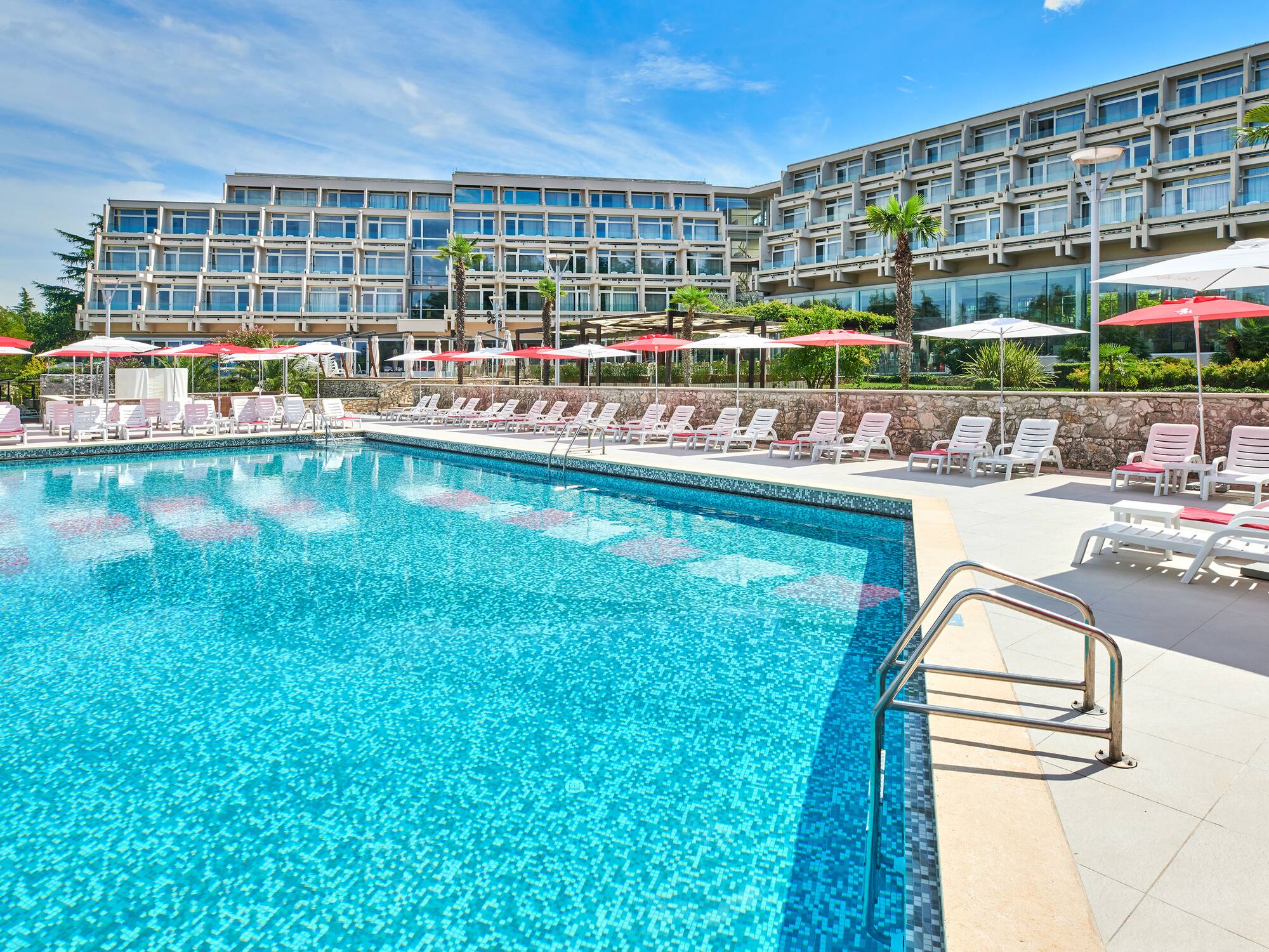 a pool with umbrellas and chairs in front of a hotel