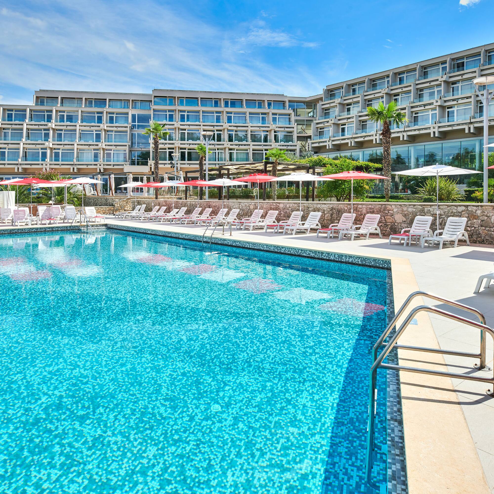 a pool with umbrellas and chairs in front of a hotel
