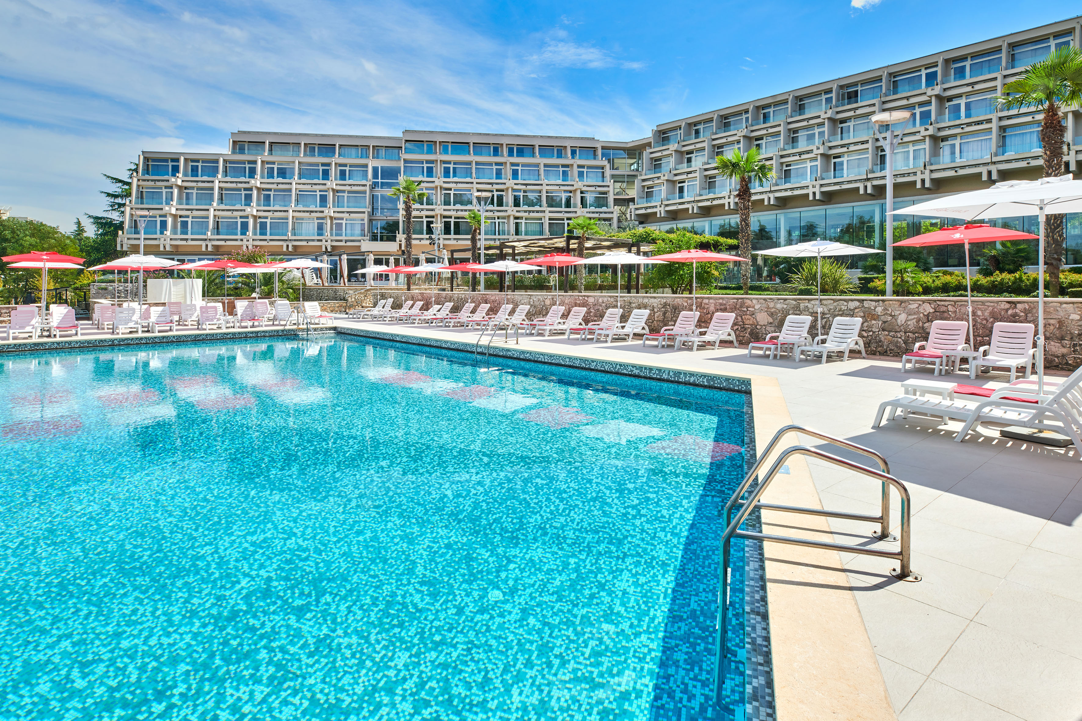 a pool with umbrellas and chairs in front of a hotel