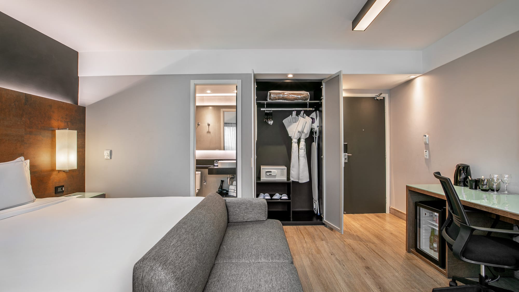Quarto de hotel moderno com cama de casal, sofá cinza, escrivaninha e armário aberto. - Deluxe Room Queen - Meliá Ibirapuera, São Paulo
