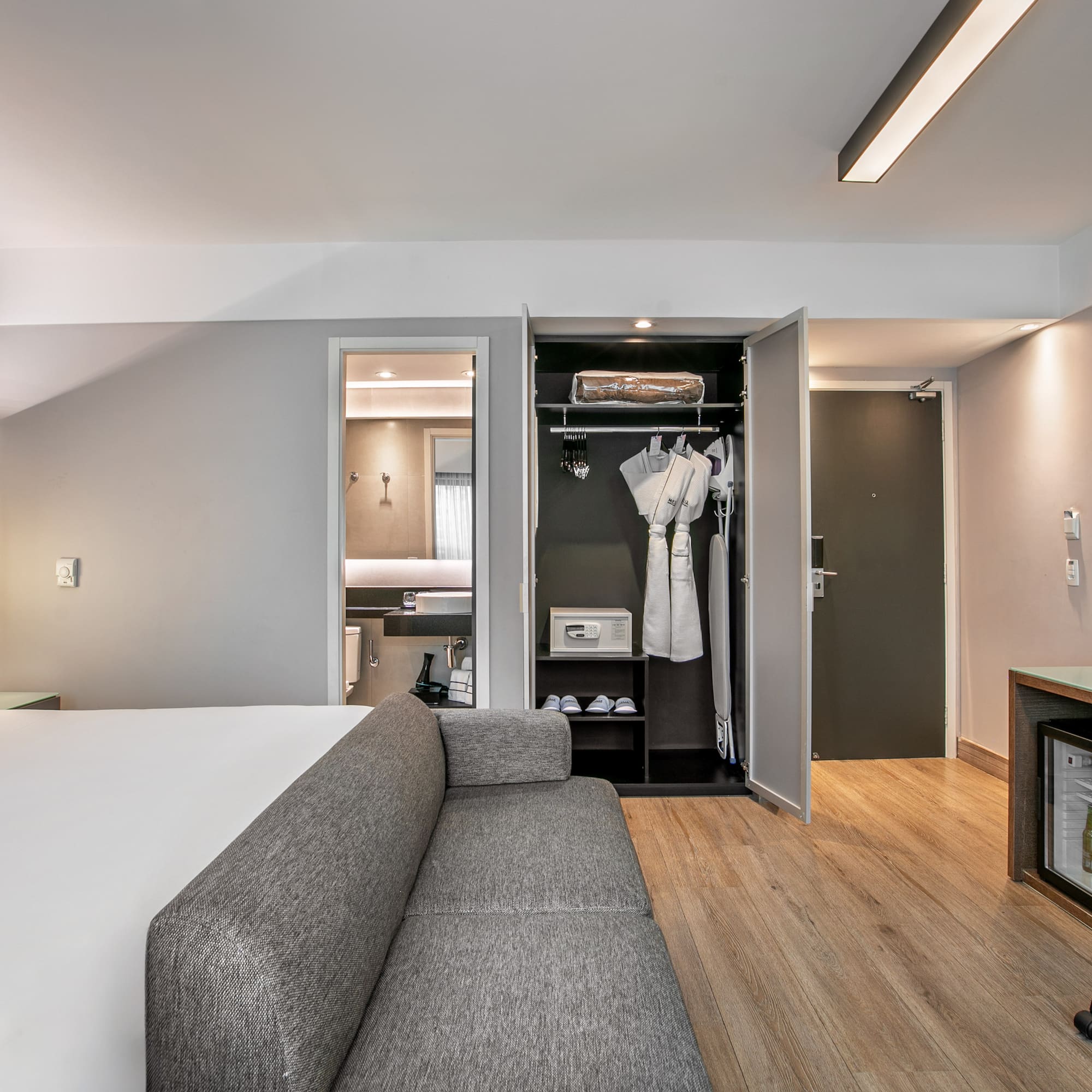 Quarto de hotel moderno com cama de casal, sofá cinza, escrivaninha e armário aberto. - Deluxe Room Queen - Meliá Ibirapuera, São Paulo