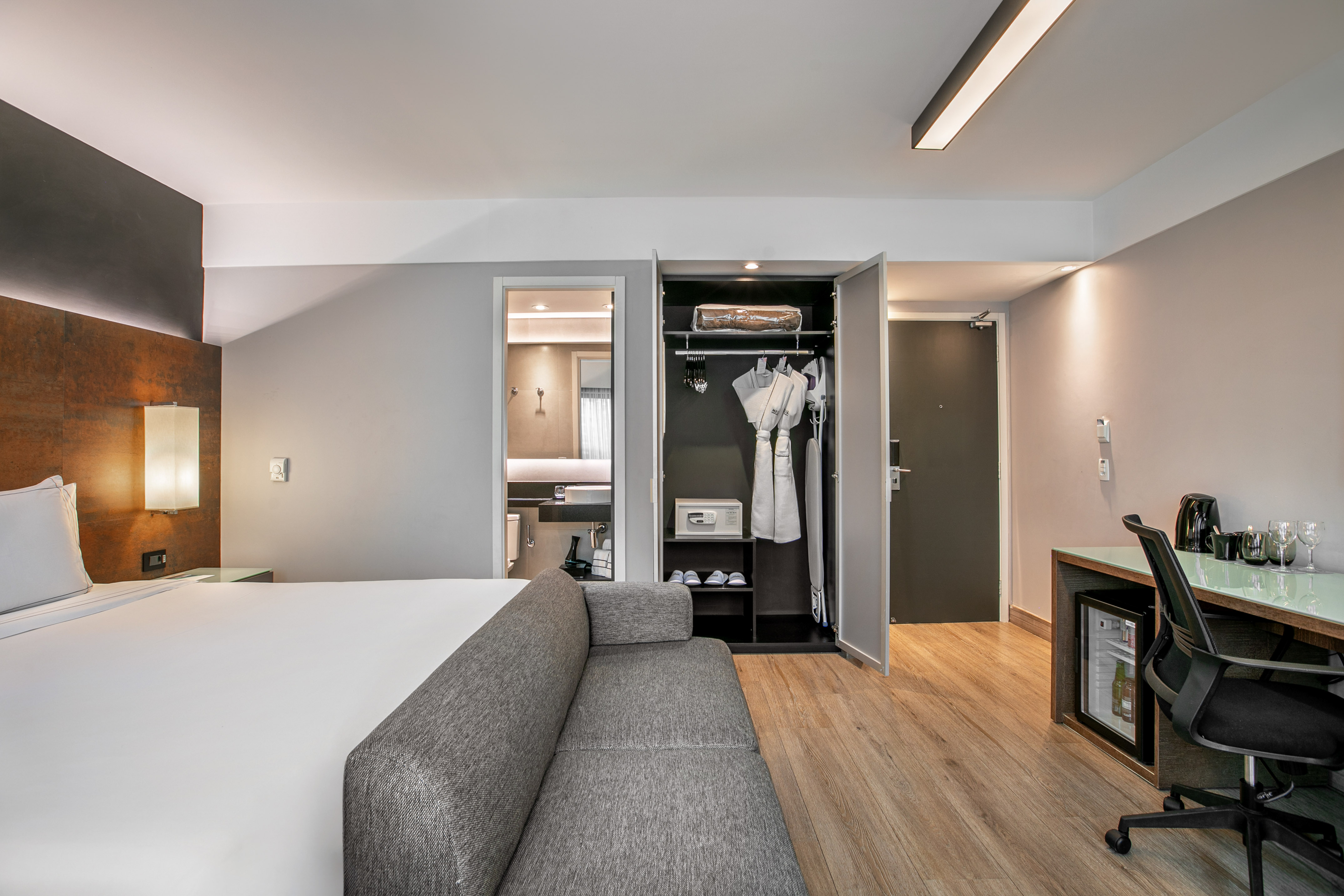 Quarto de hotel moderno com cama de casal, sofá cinza, escrivaninha e armário aberto. - Deluxe Room Queen - Meliá Ibirapuera, São Paulo