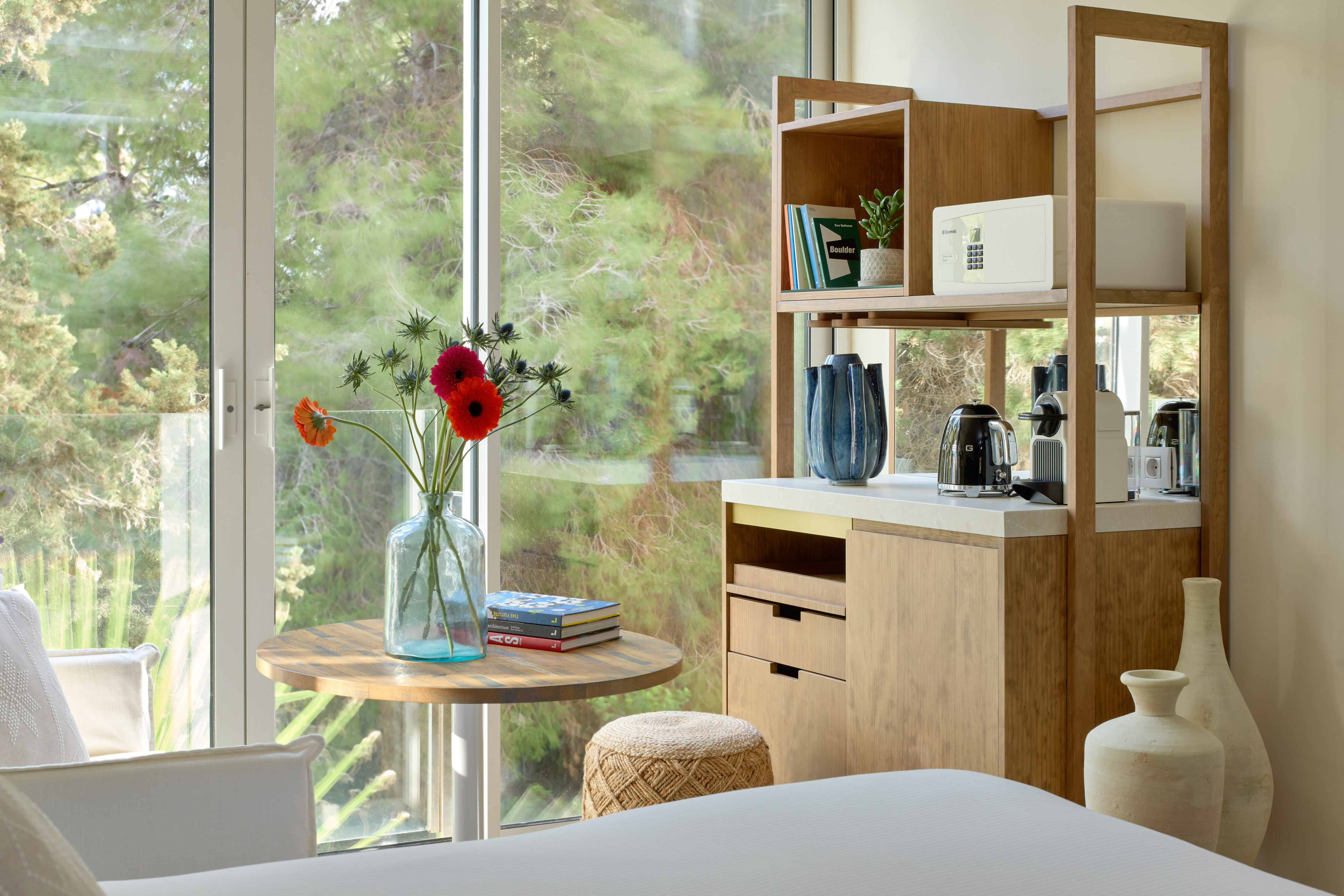 Bright hotel room with mini-bar, coffee machine, fresh flowers, and forest view.