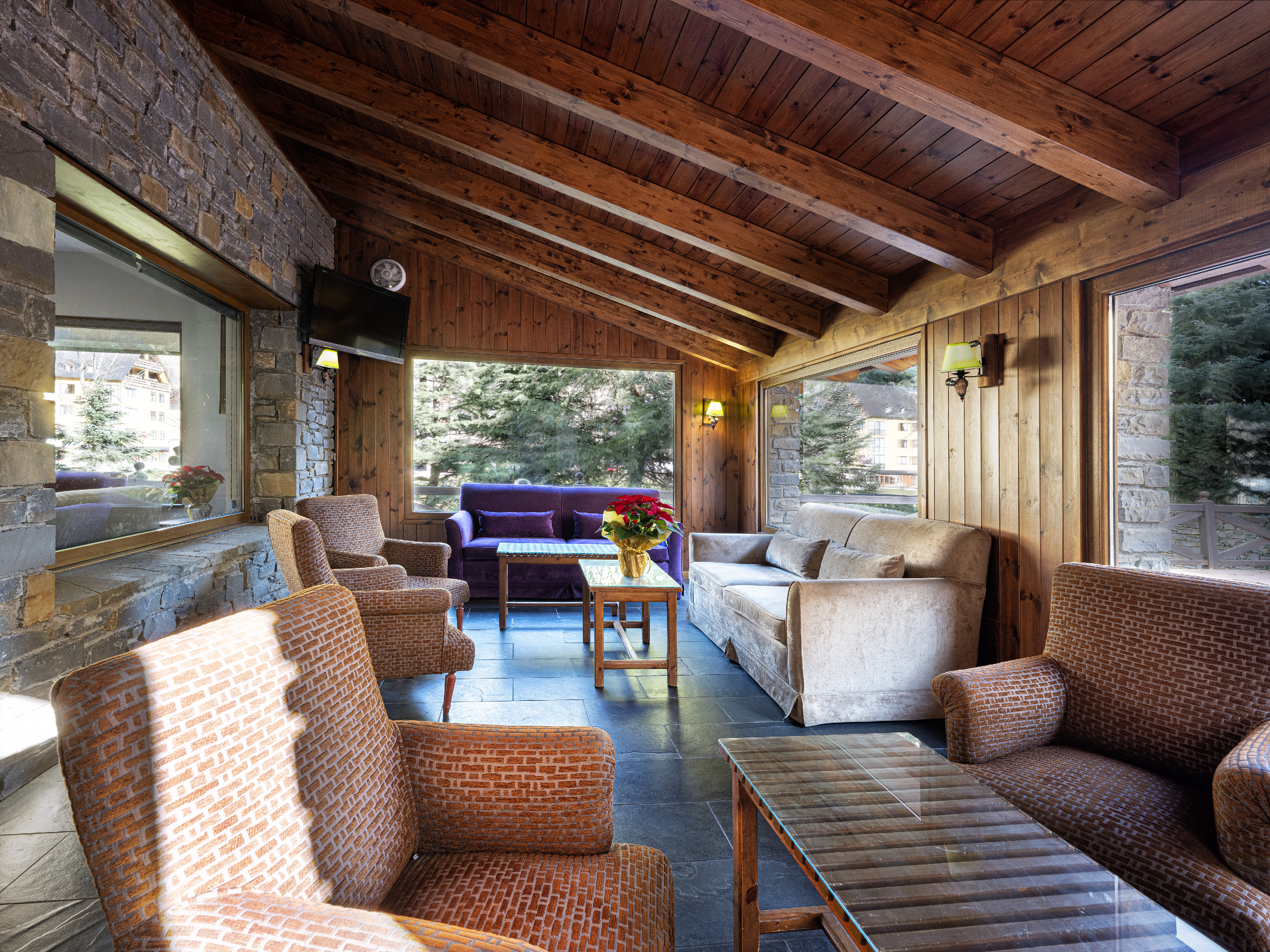 Rustic lodge lounge with wooden ceiling, stone walls, and scenic window views.