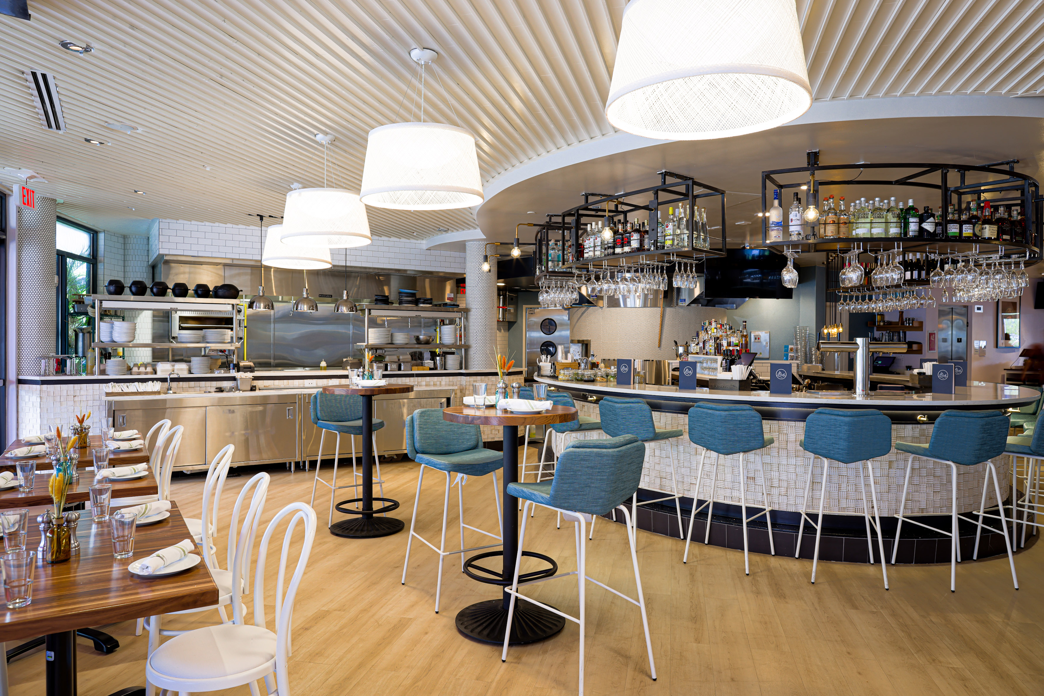 Modern restaurant bar and dining area with teal stools and open kitchen.