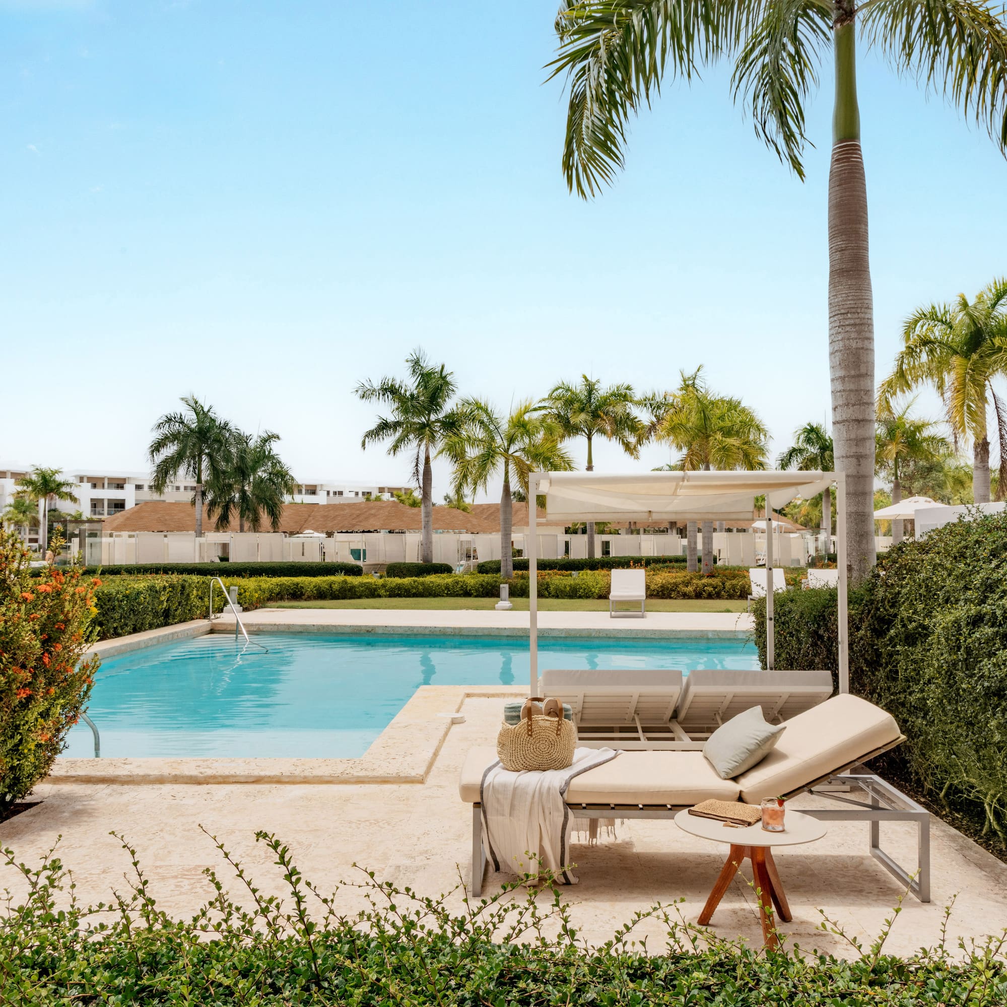 Tropical resort pool, daybeds, palm trees, and lush green landscaping.