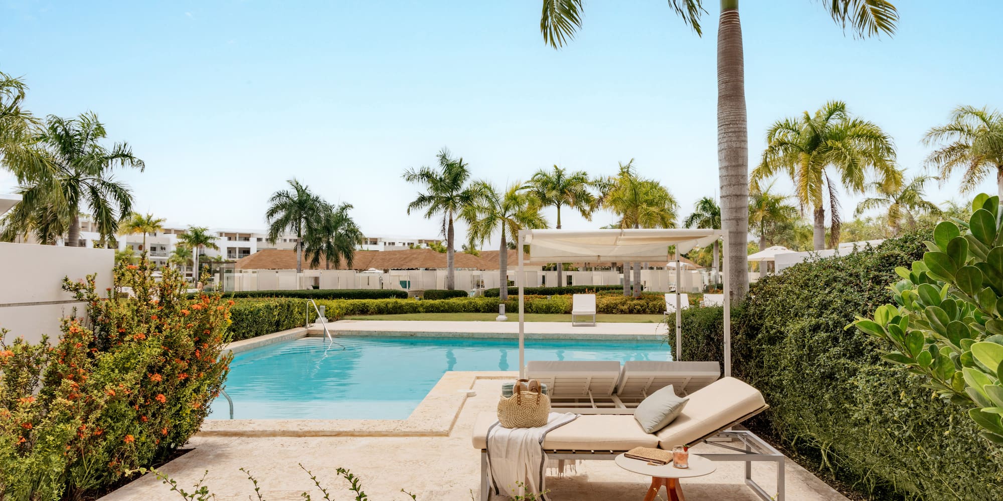 Tropical resort pool with lounge chairs, palm trees, and lush greenery.