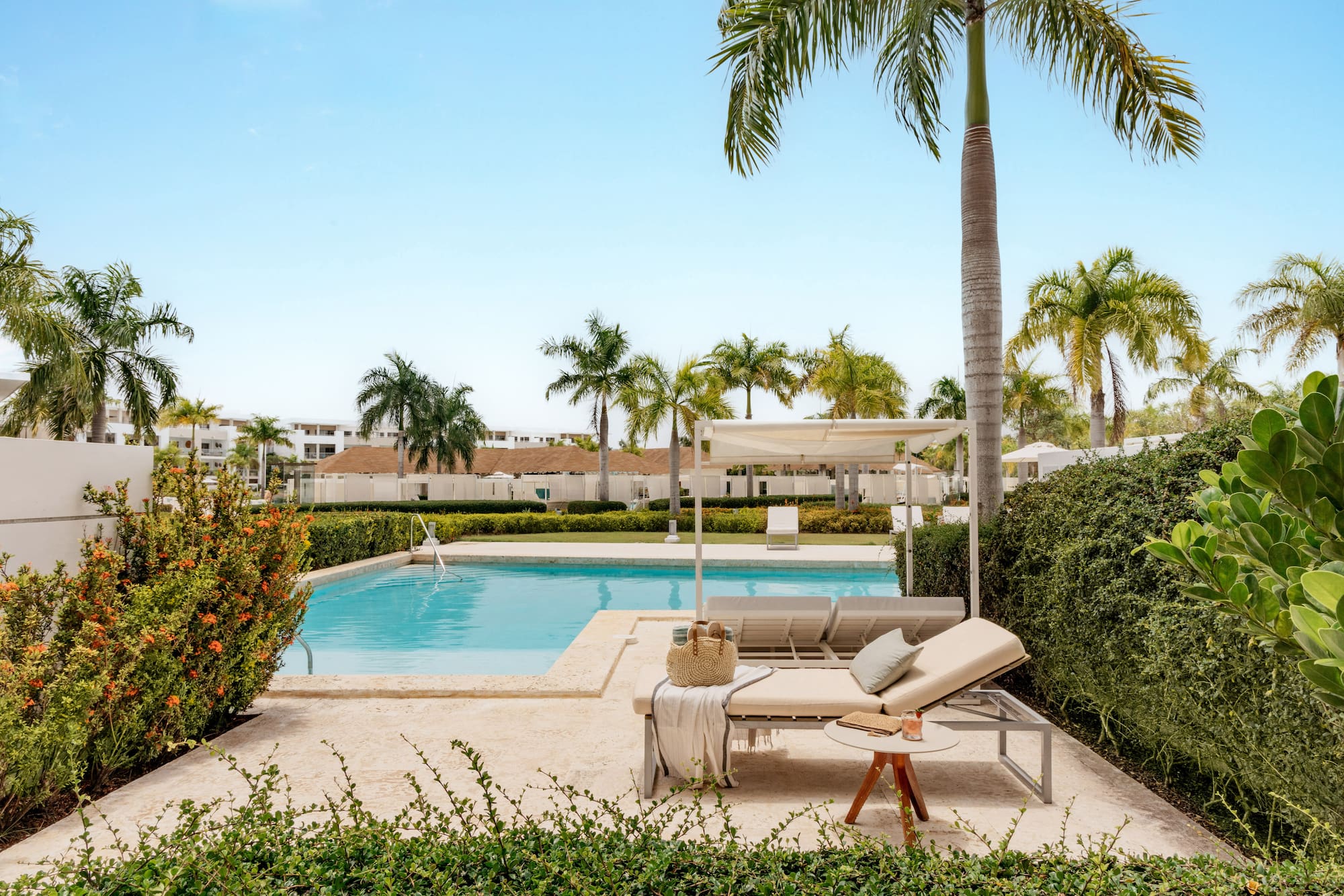 Tropical resort pool, daybeds, palm trees, and lush green landscaping.
