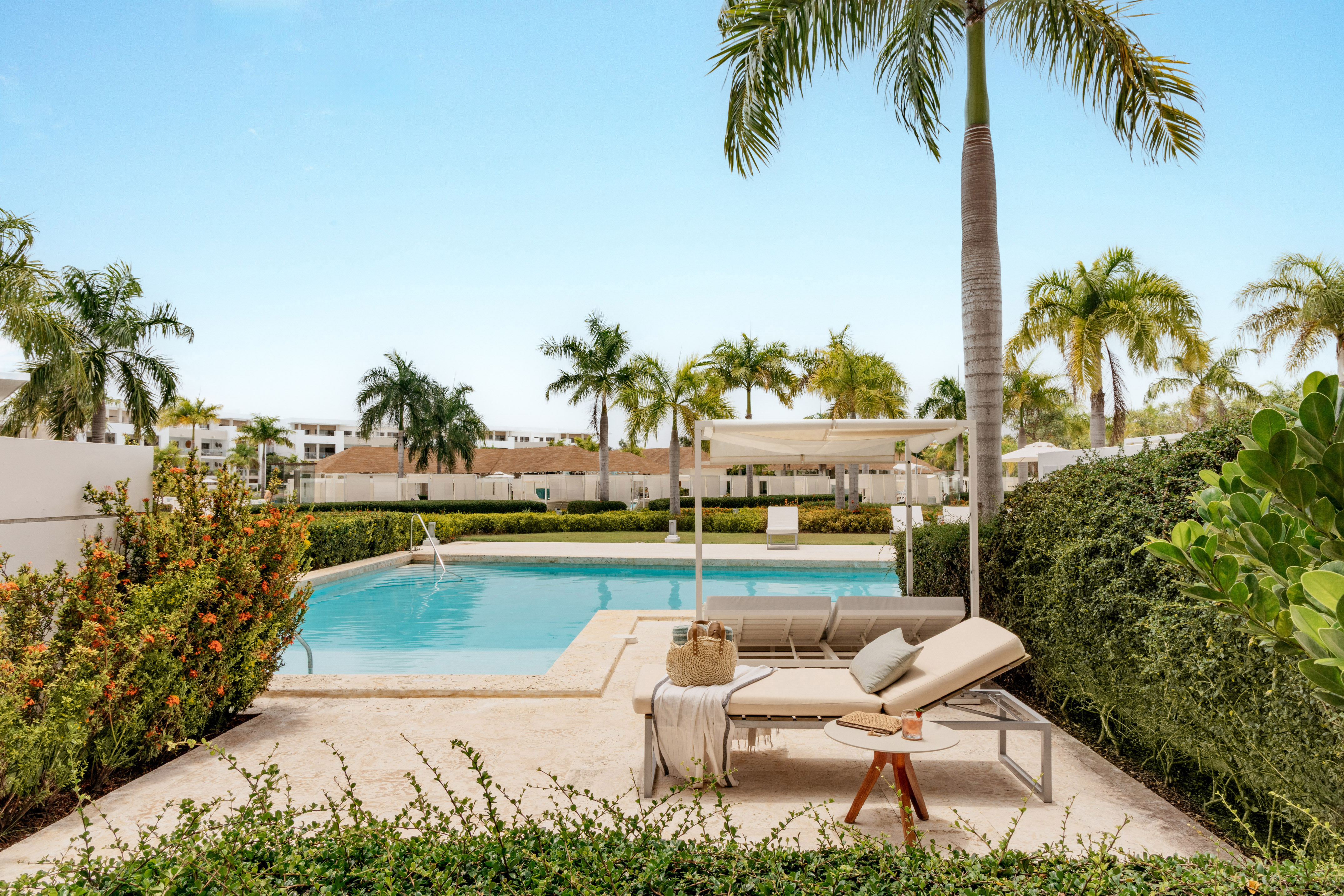 Tropical resort pool, daybeds, palm trees, and lush green landscaping.