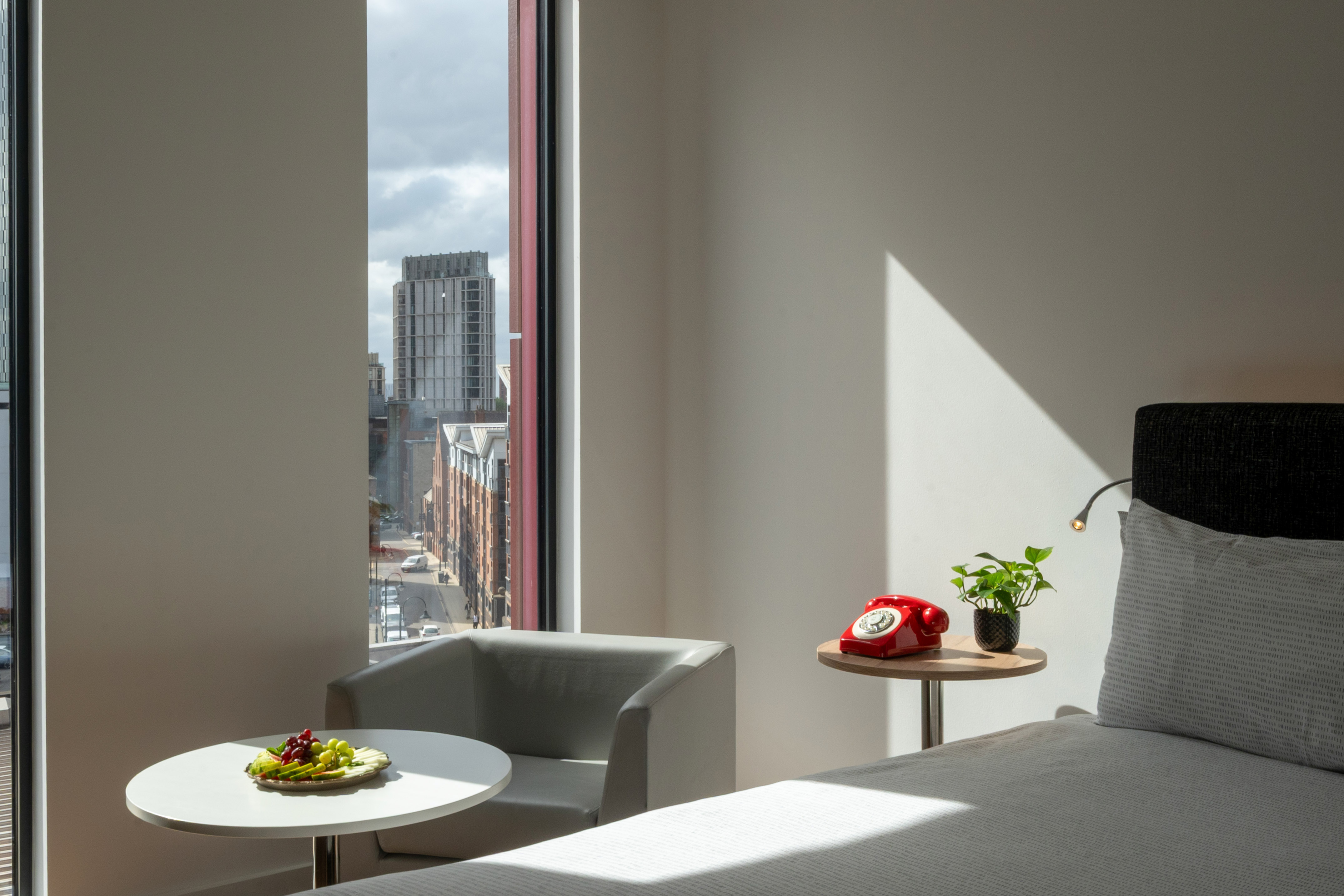 Modern hotel bedroom with city view, fruit plate, and red rotary phone.