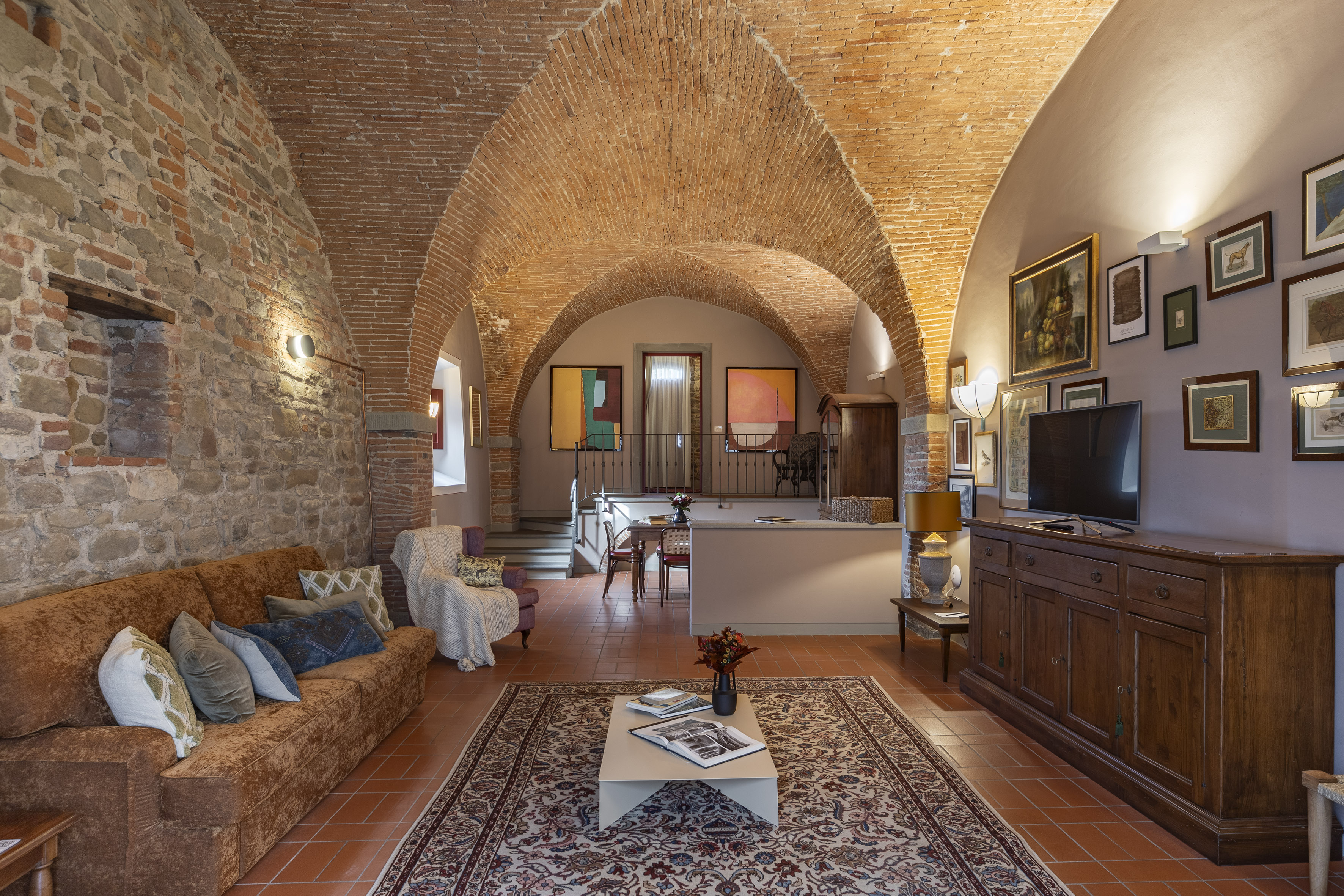 Rustic living room with vaulted brick ceiling, stone walls, and terracotta floor.