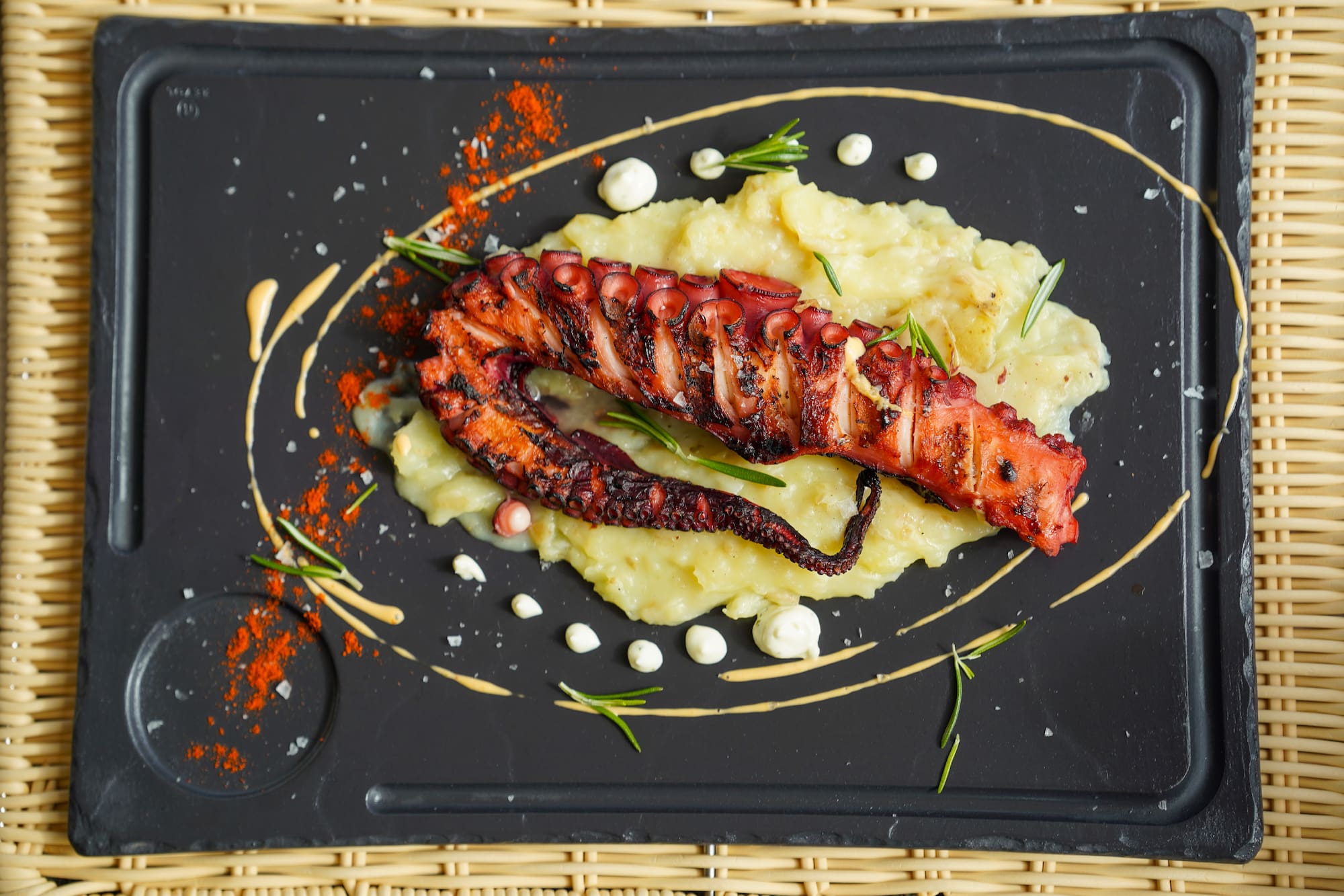 Pulpo a la parrilla, puré, romero y pimentón en plato de pizarra negra.