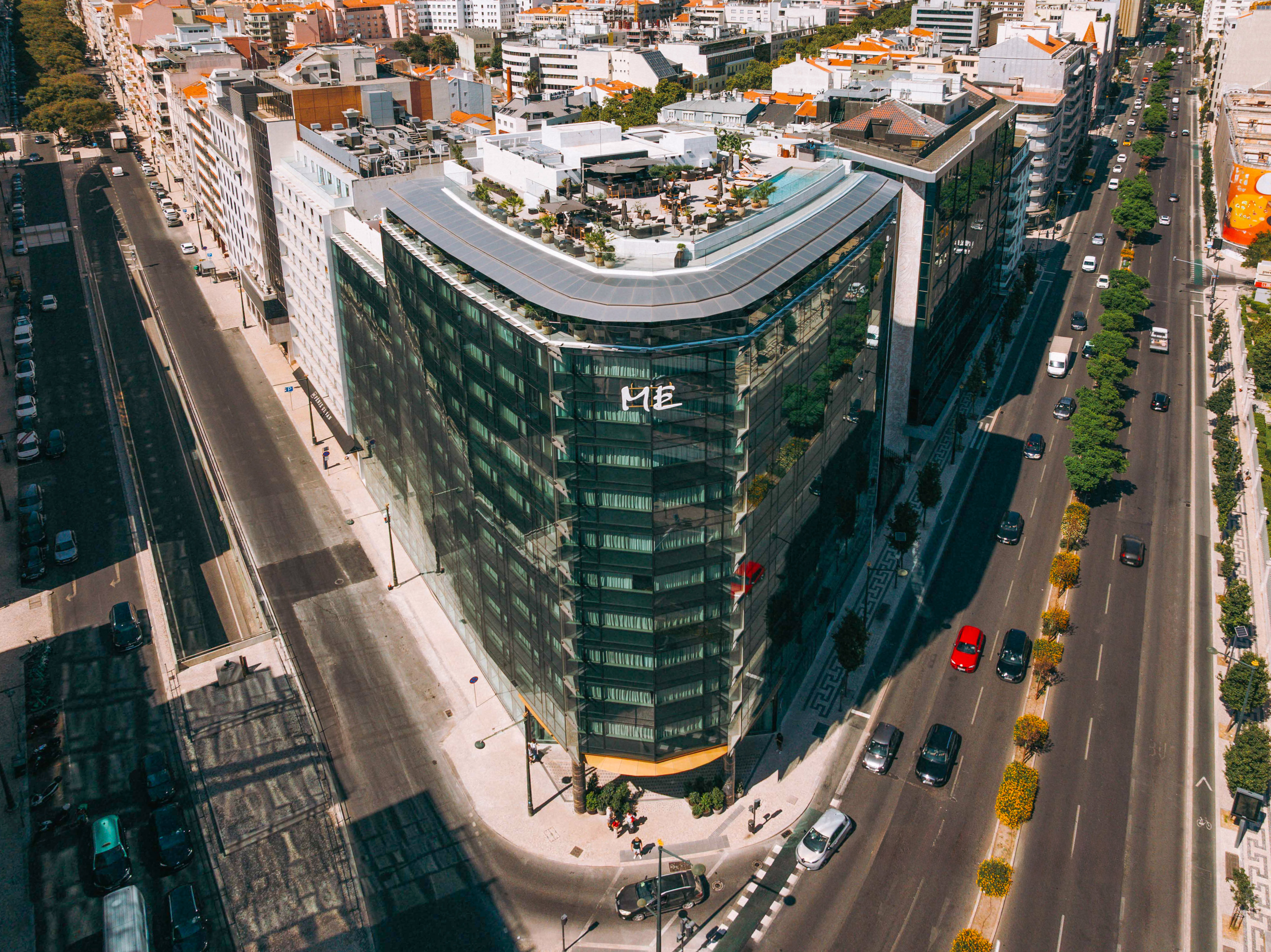 ME Lisbon hotel: modern glass building with rooftop pool, urban street view.