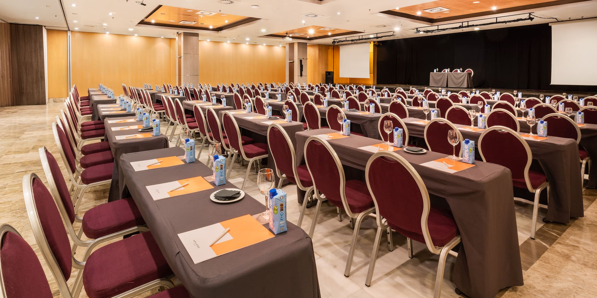 Empty conference room with rows of tables, red chairs, and projector screen.