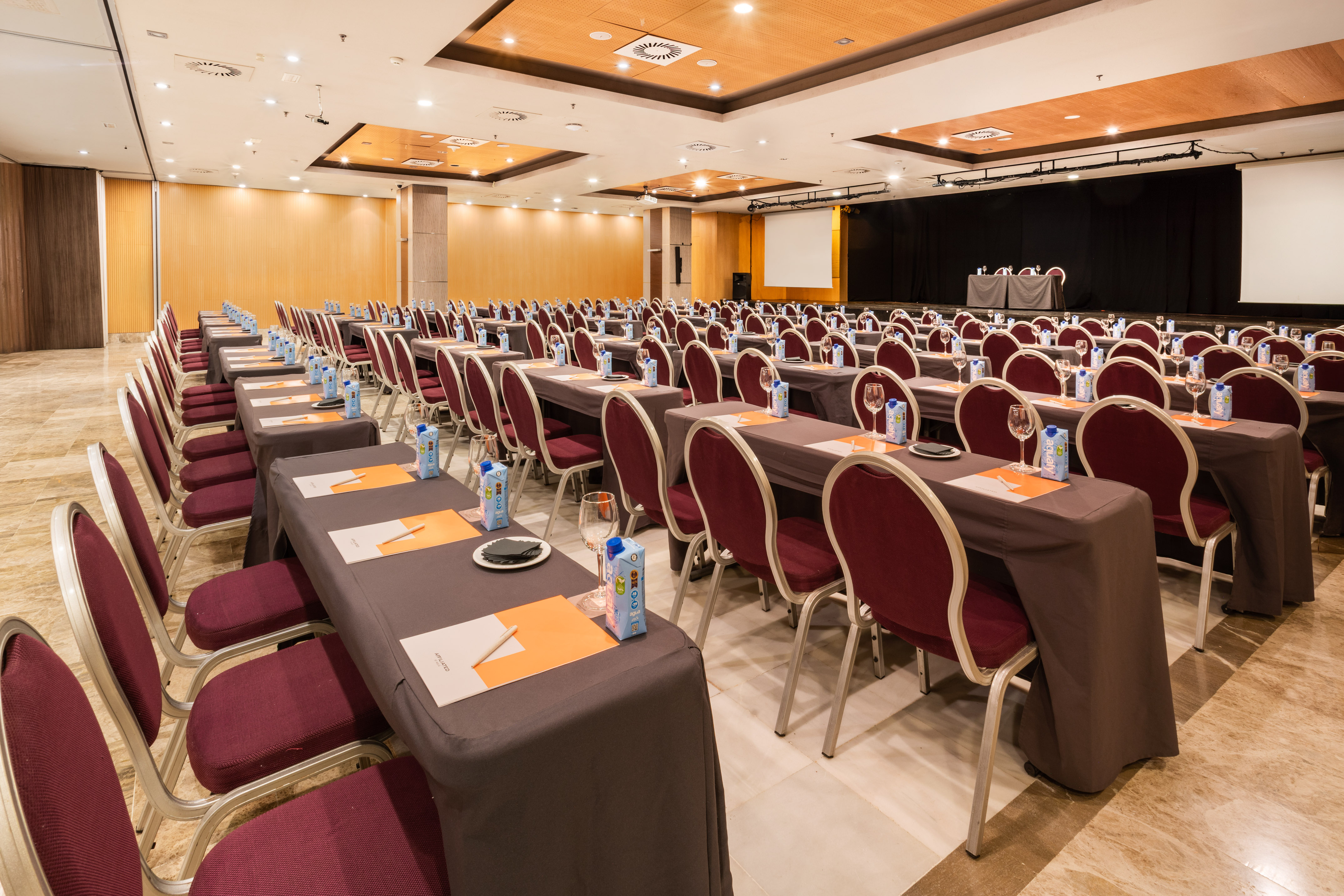 Empty conference room with rows of tables, red chairs, and projector screen.